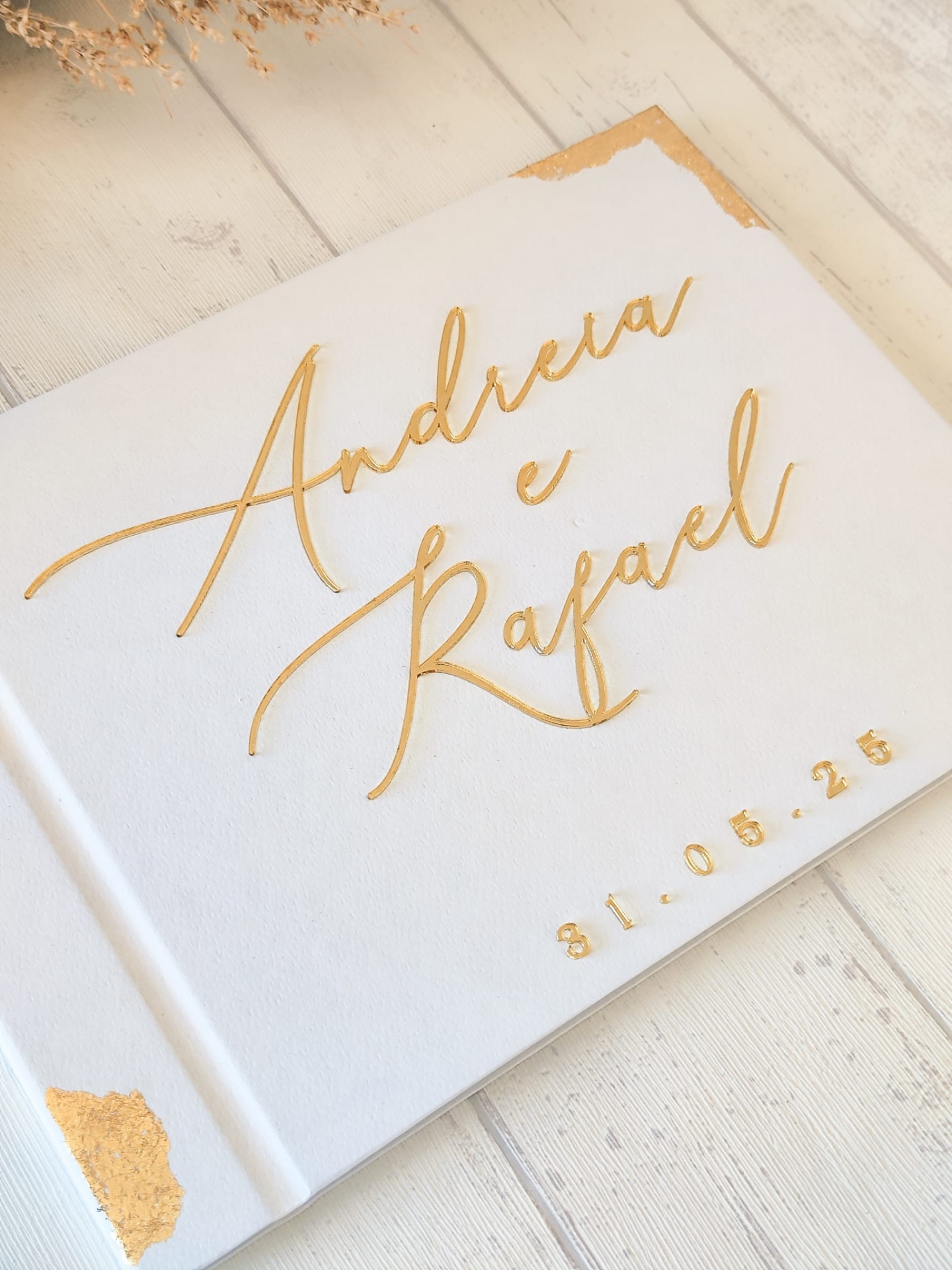 Livro branco com nomes Andreia e Rafael em dourado e data 31.05.25