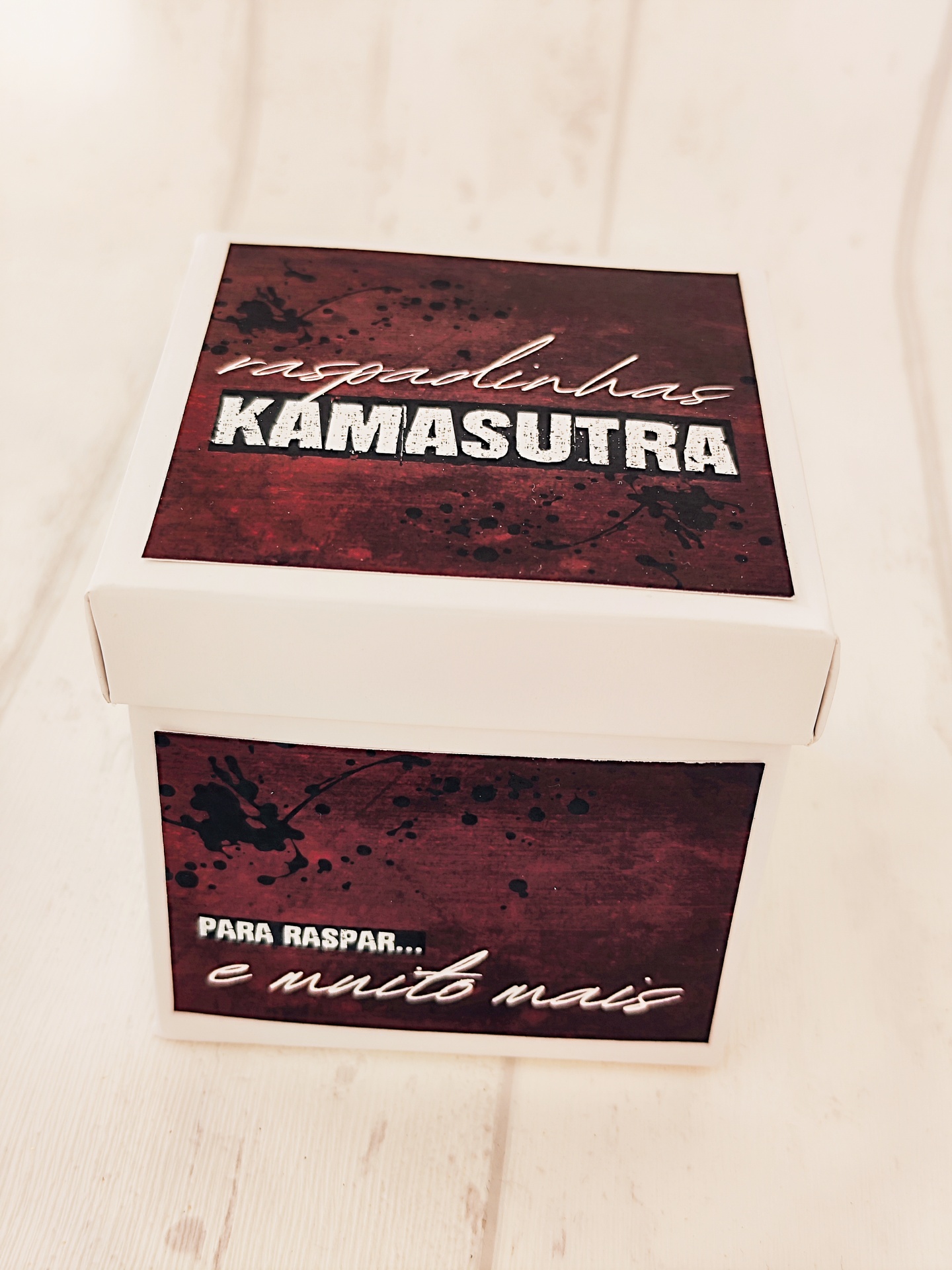 Caixa branca para raspar com texto KAMASUTRA e frases promocionais.