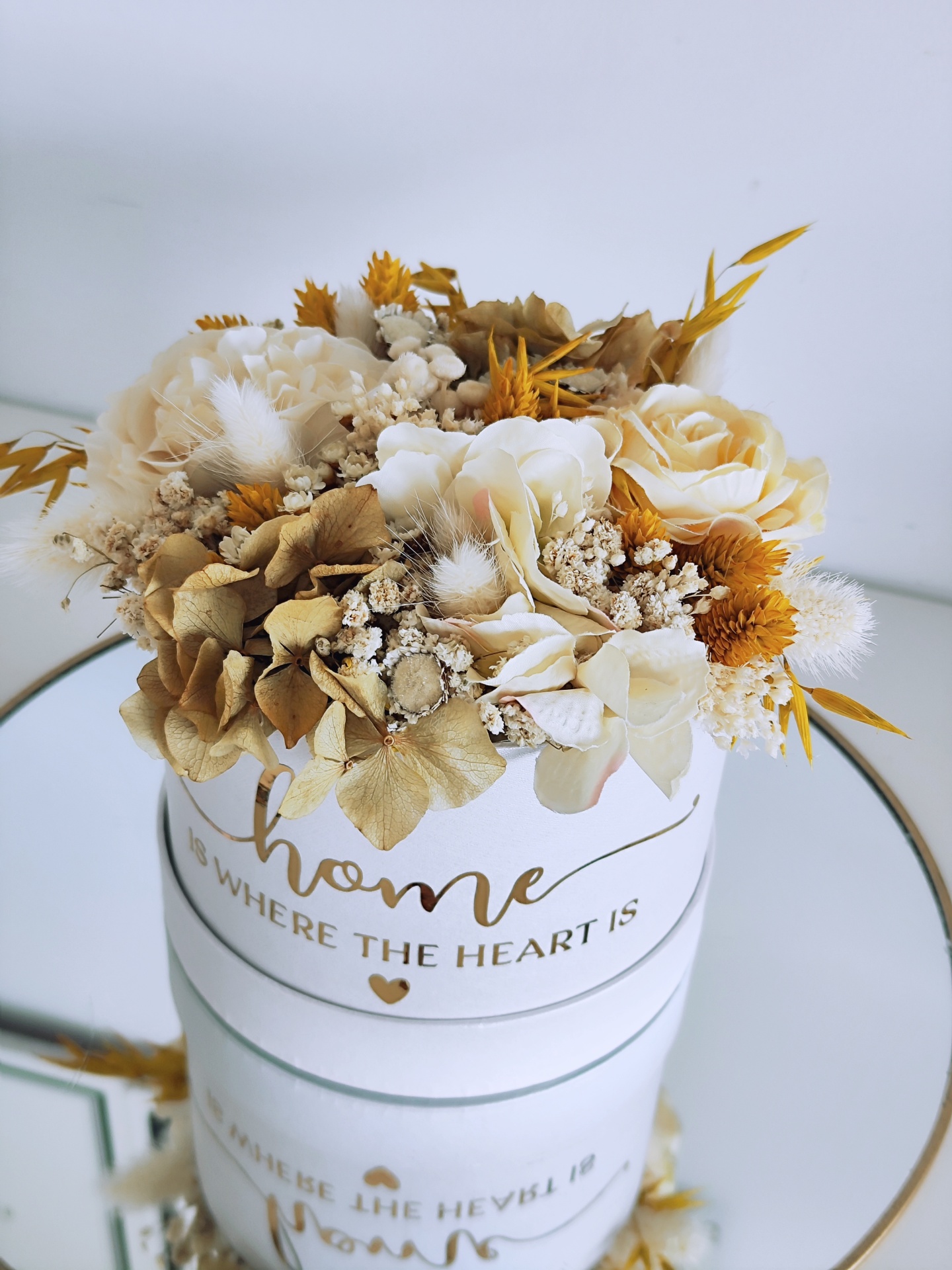 Arranjo de flores secas em vaso branco com frase dourada sobre espelho redondo