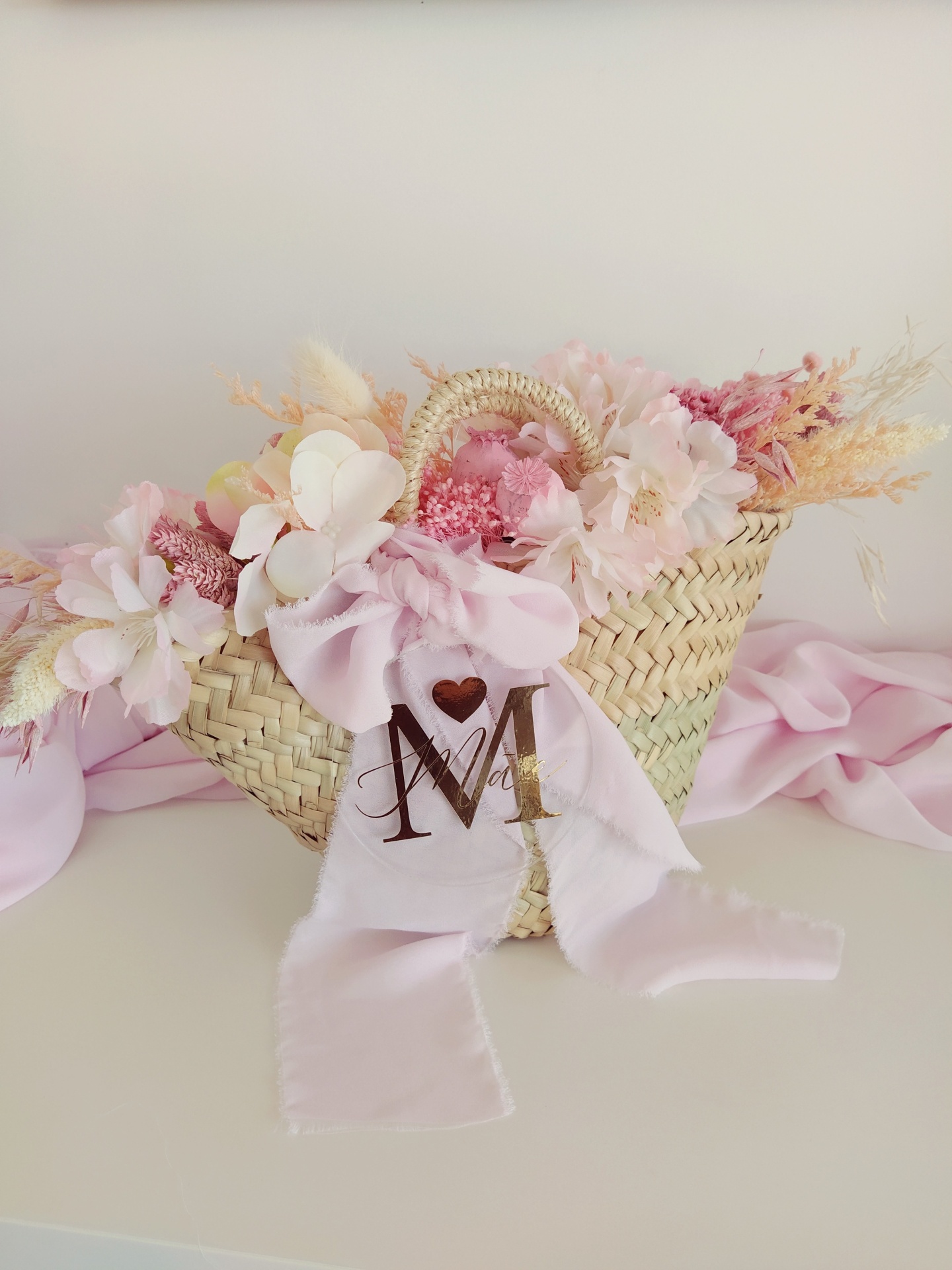 Cesta de palha com flores artificiais rosa e fita decorativa rosa com letra M