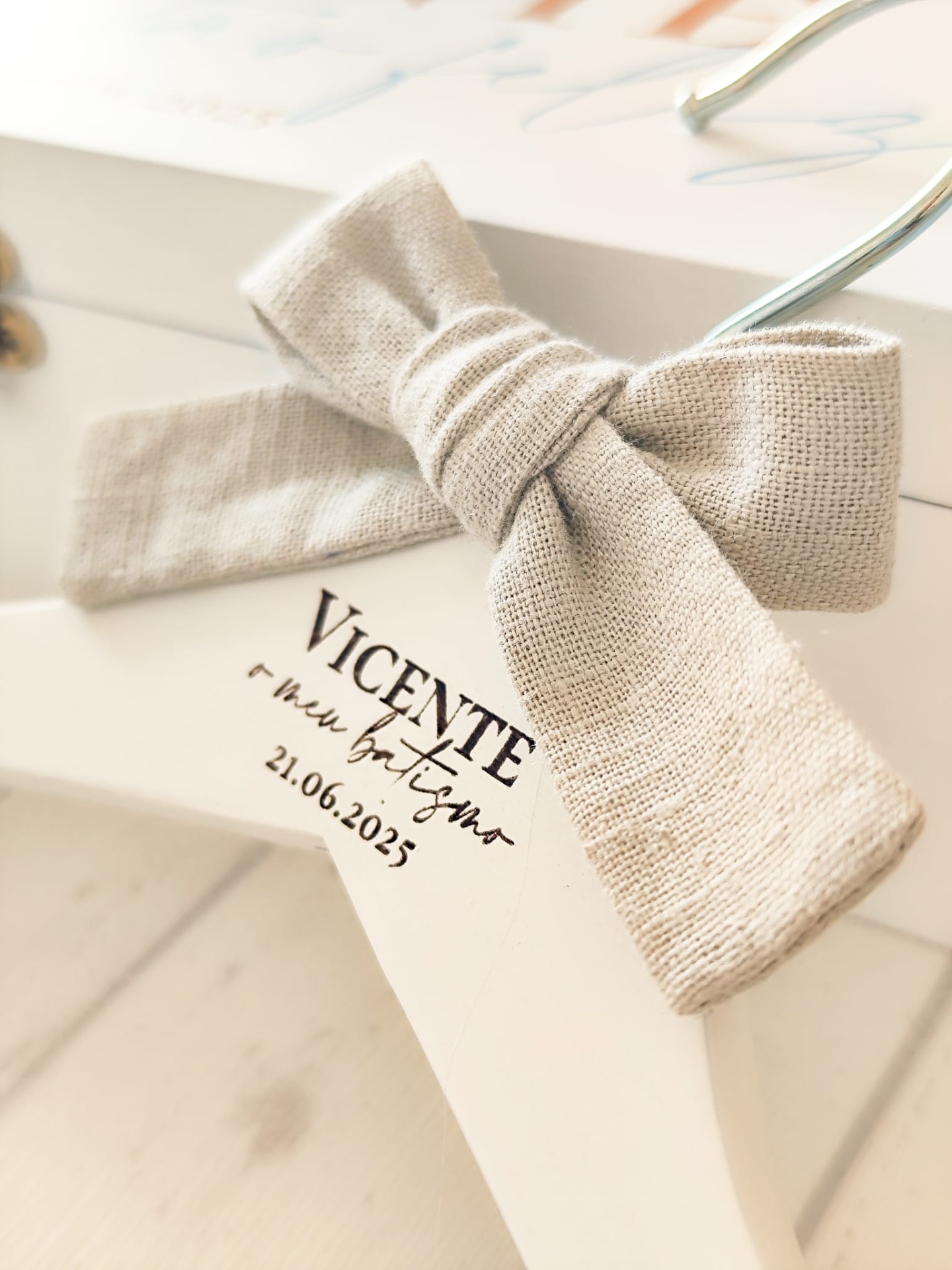 Cabide branco de madeira com laço bege e texto personalizado em preto.