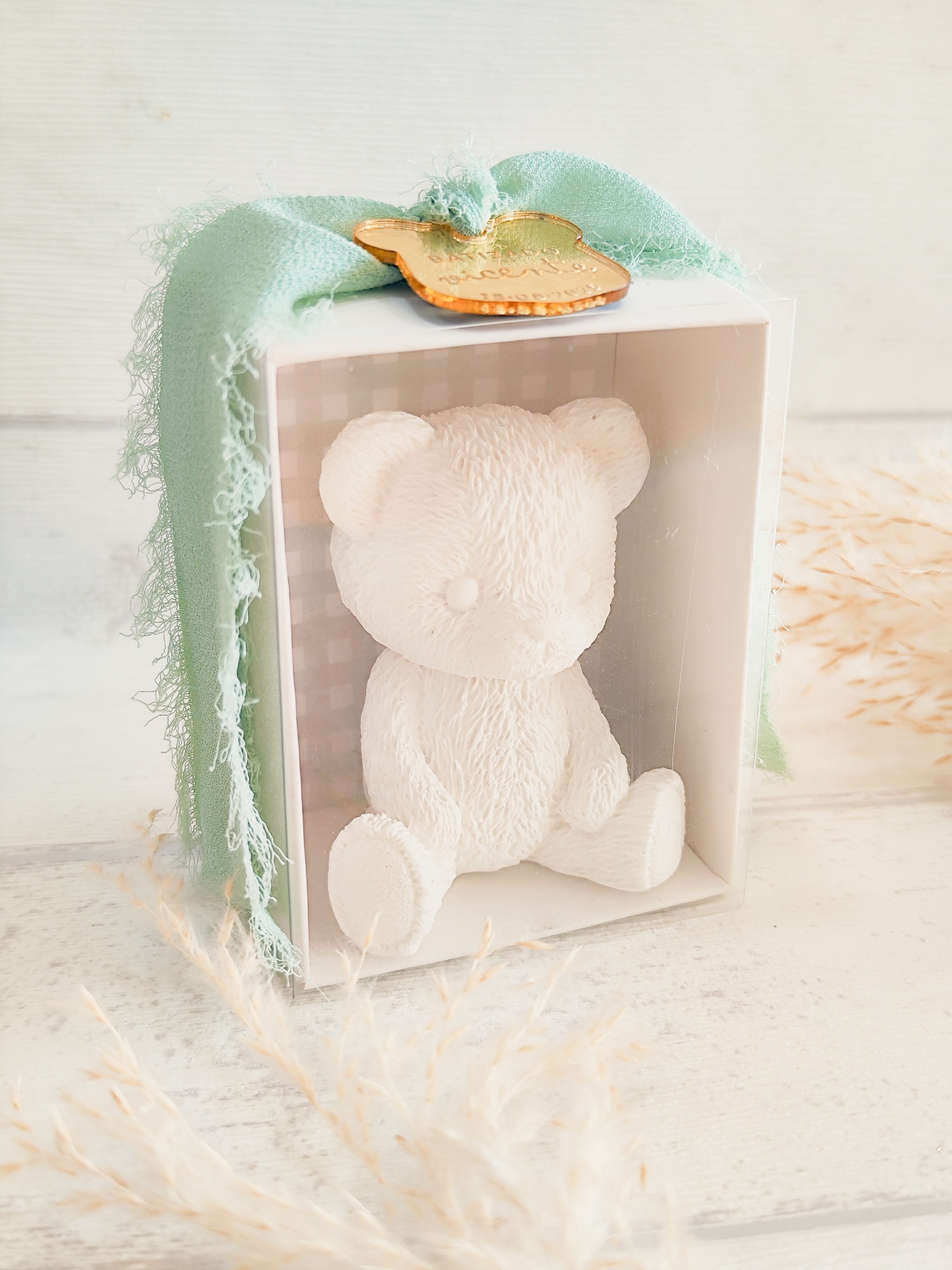 Urso decorativo branco dentro de caixa branca com fita verde