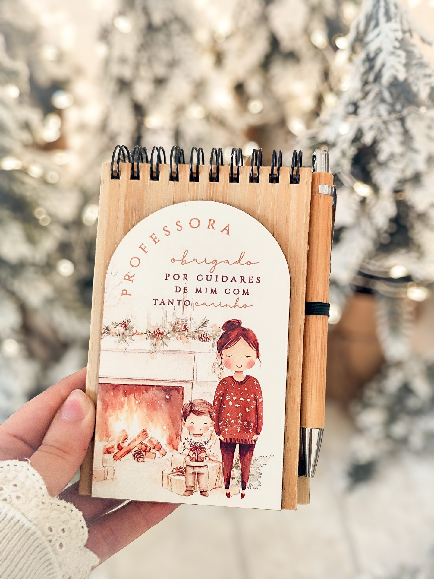 Bloco de notas em madeira com desenho de lareira e personagens, texto dedicado a professora, caneta de madeira ao lado.