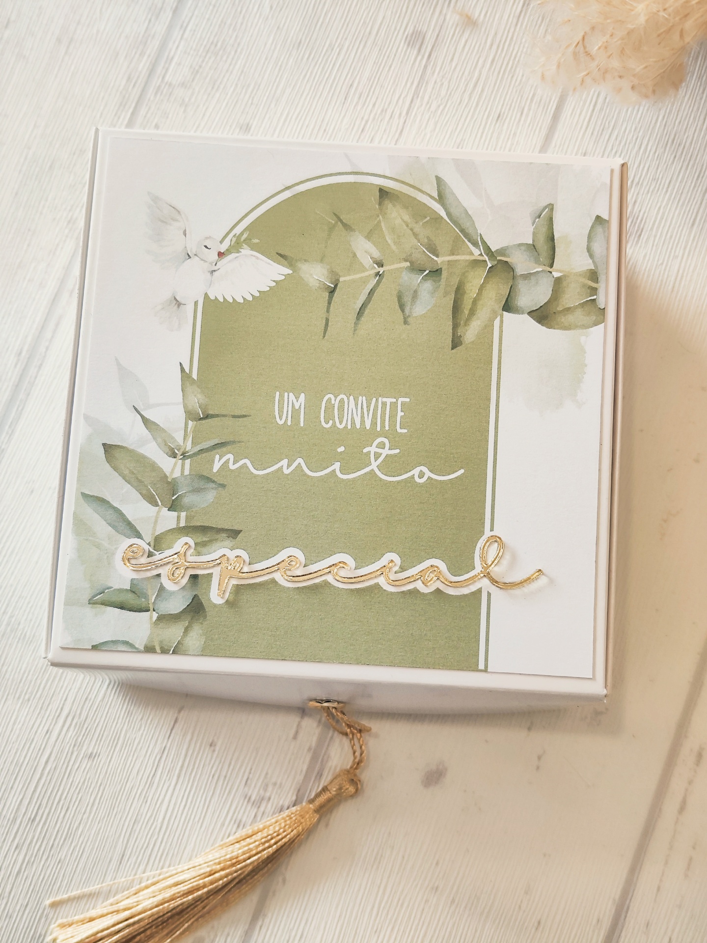 Caixa branca decorada com convite especial, folhas verdes e pomba