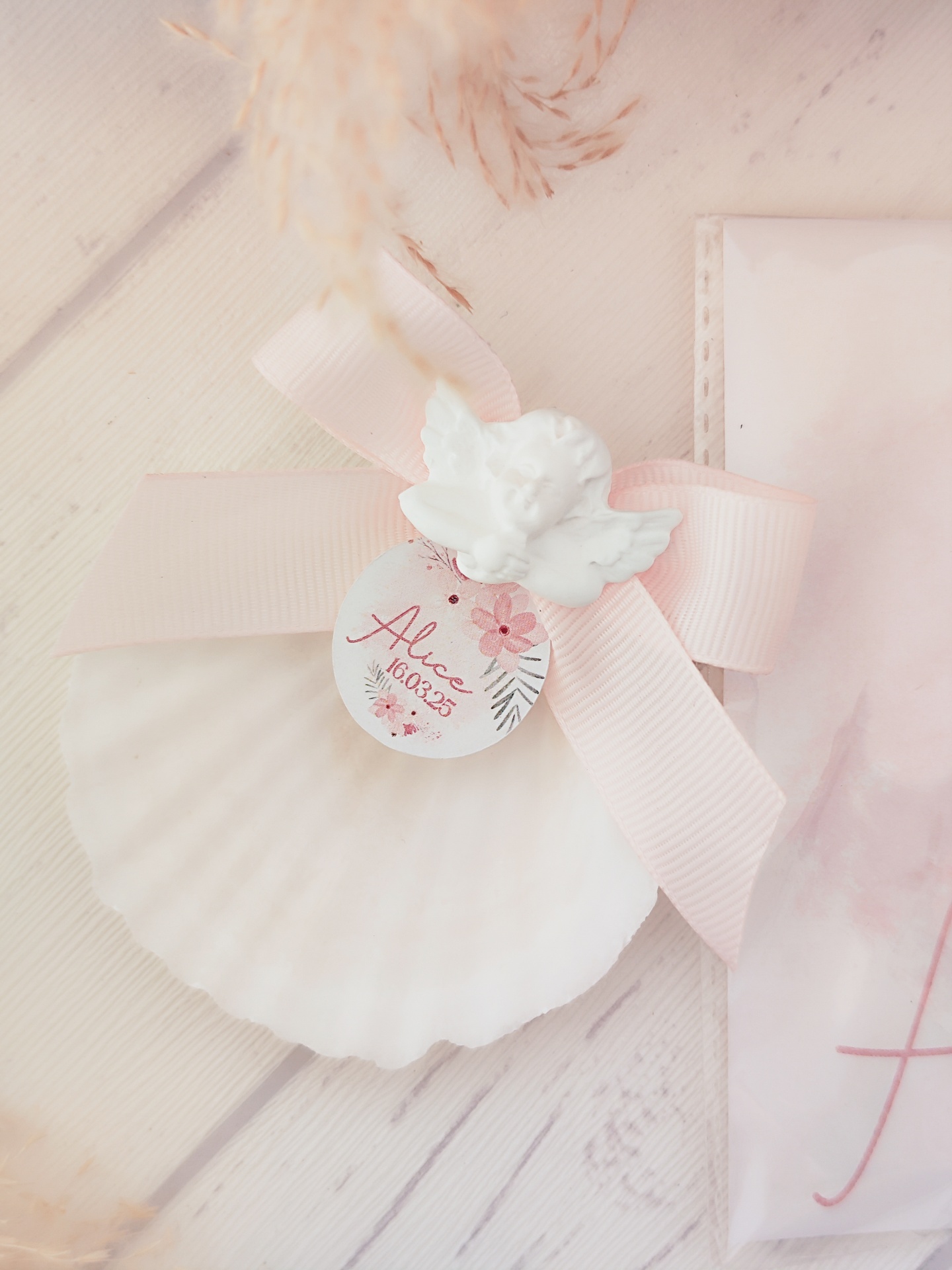 Concha branca com laço rosa, anjo e etiqueta com texto Alice 10.07.23
