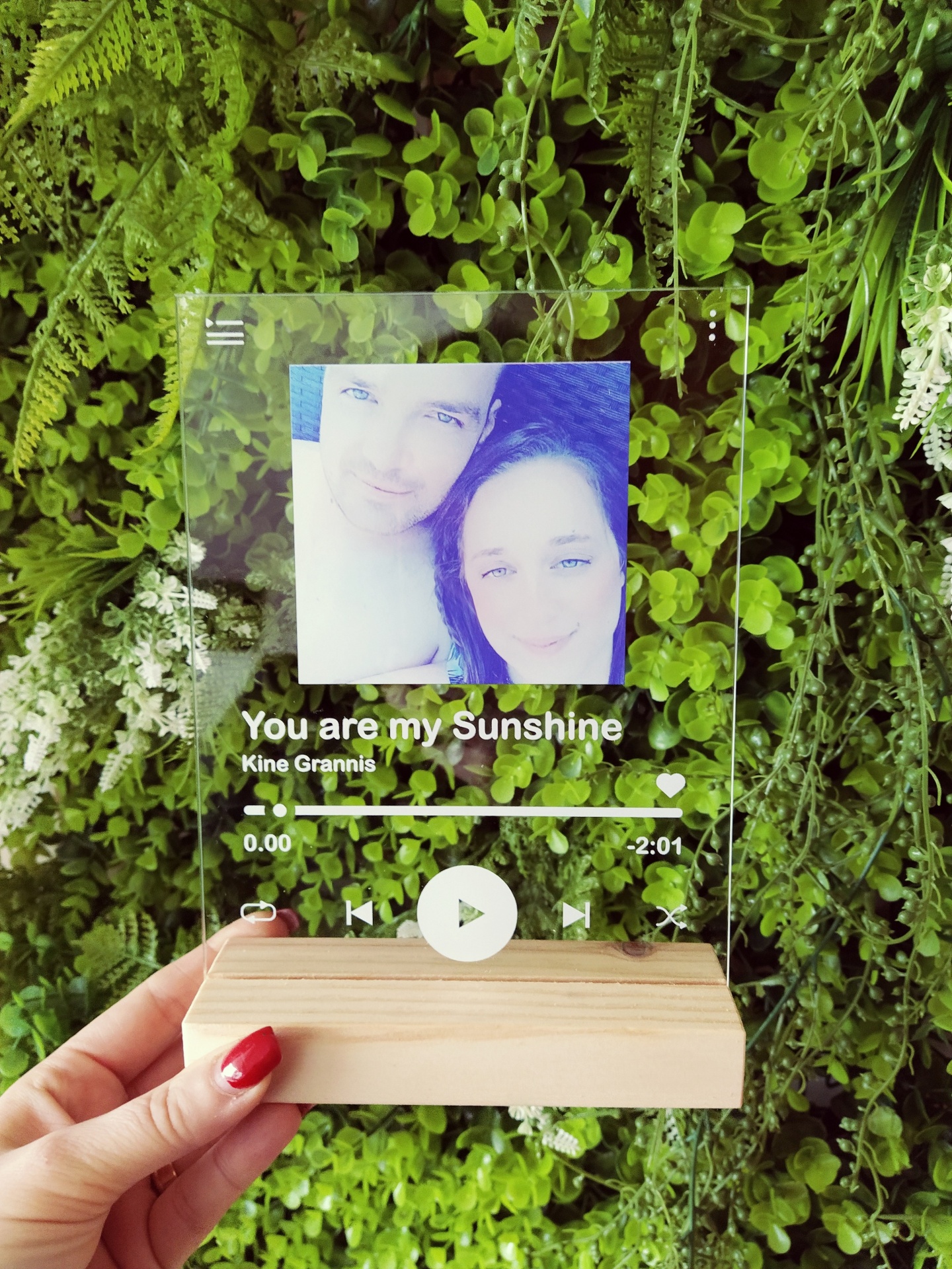 Placa decorativa em acrílico com base de madeira mostrando foto e texto, em fundo de plantas verdes