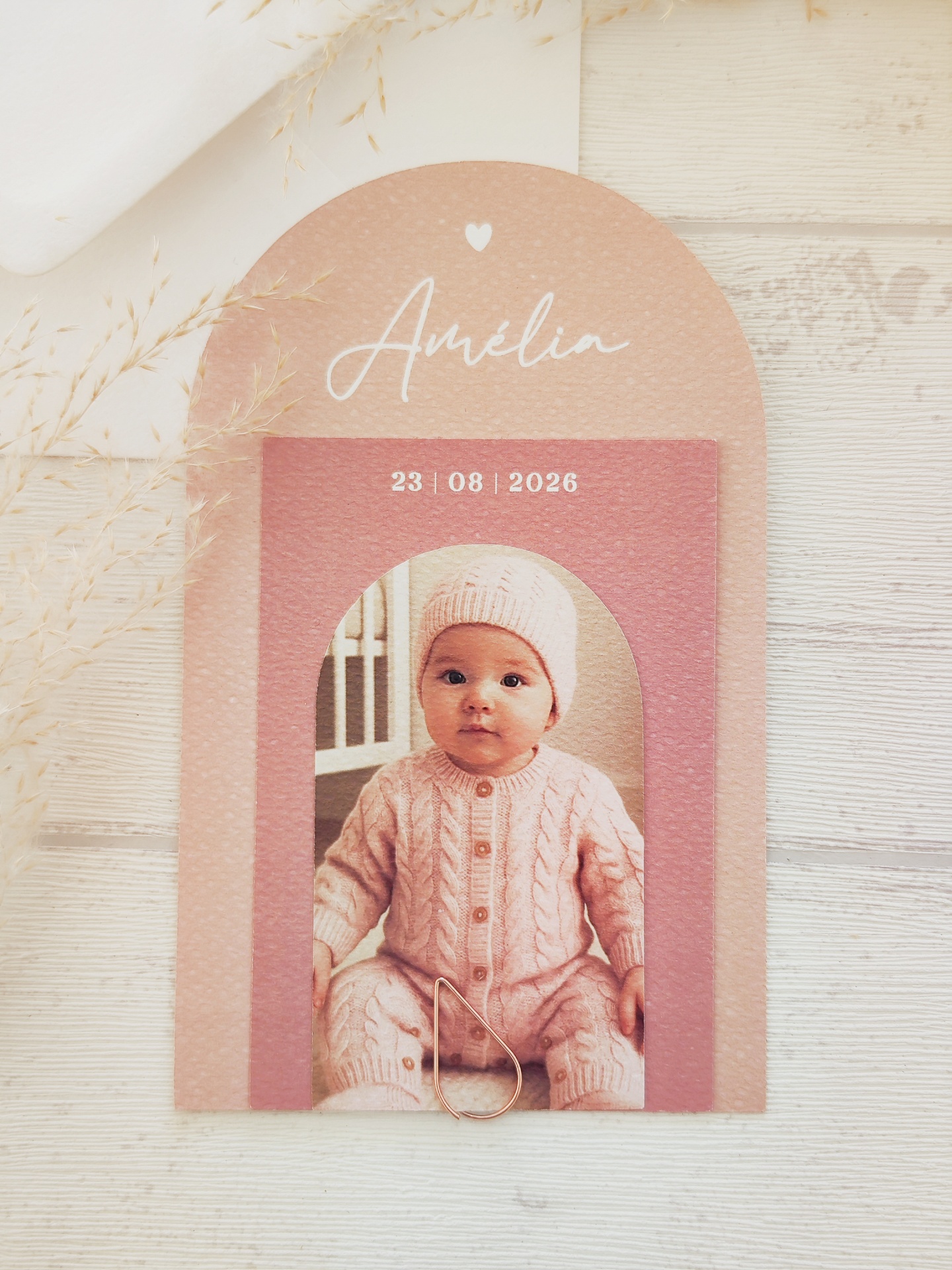 Convite de papel decorado com foto de bebé vestindo roupa rosa e texto Amélia 23 08 2026.