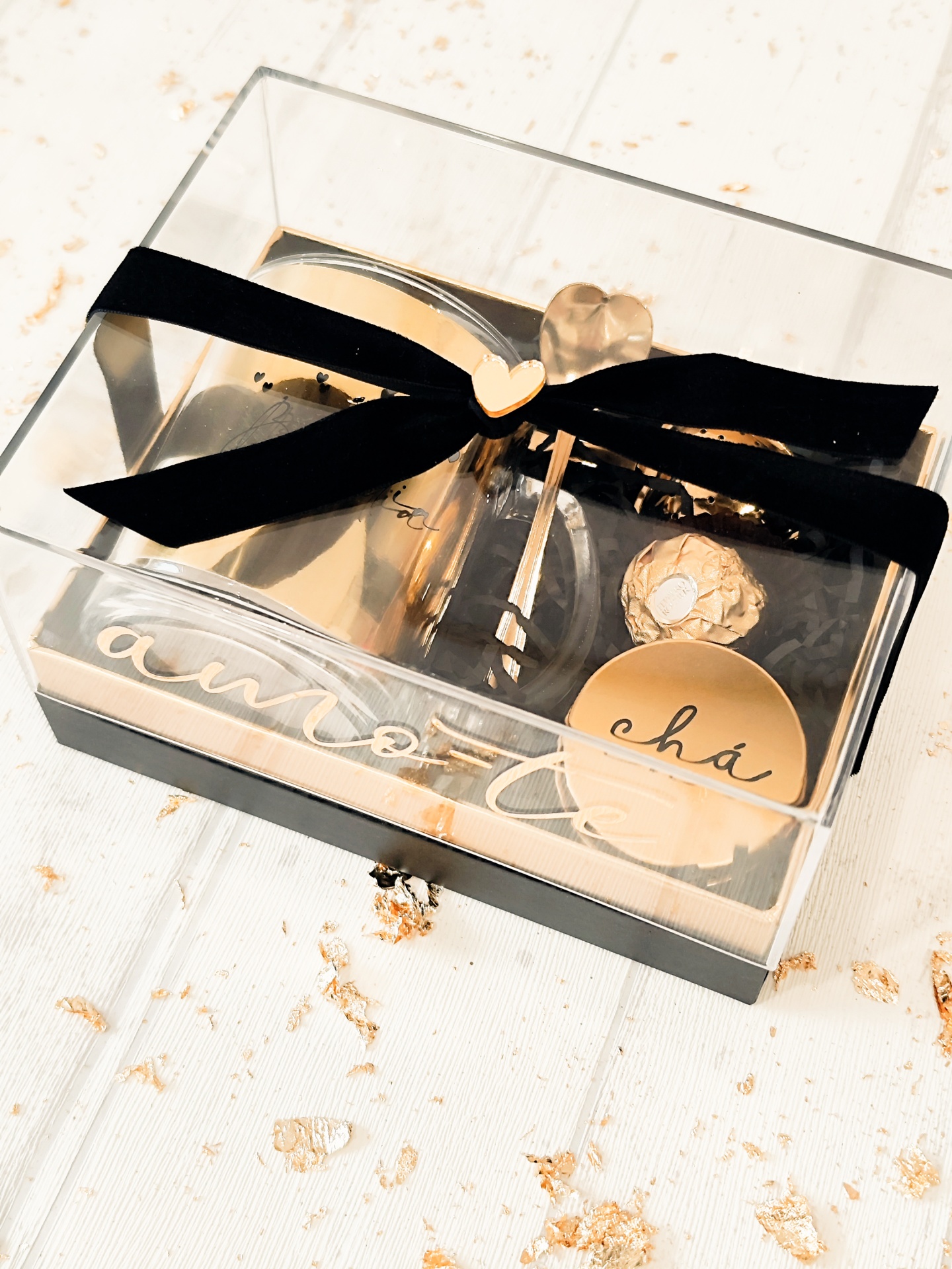 Conjunto presente para chá em caixa transparente com laço preto e medalha em forma de coração.