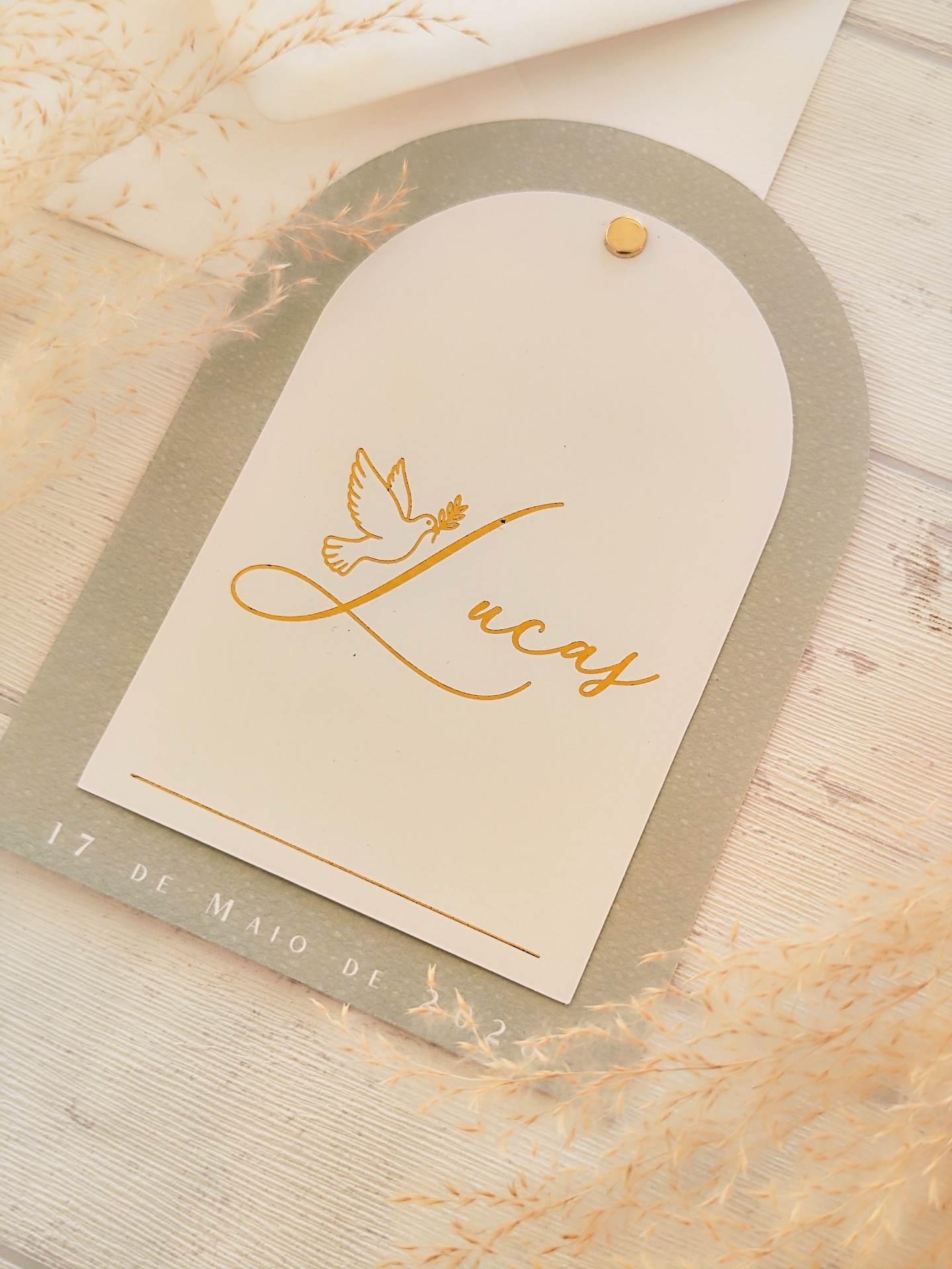 Convite ou cartão com nome Lucas, pomba e data numa superfície de madeira com ramos secos