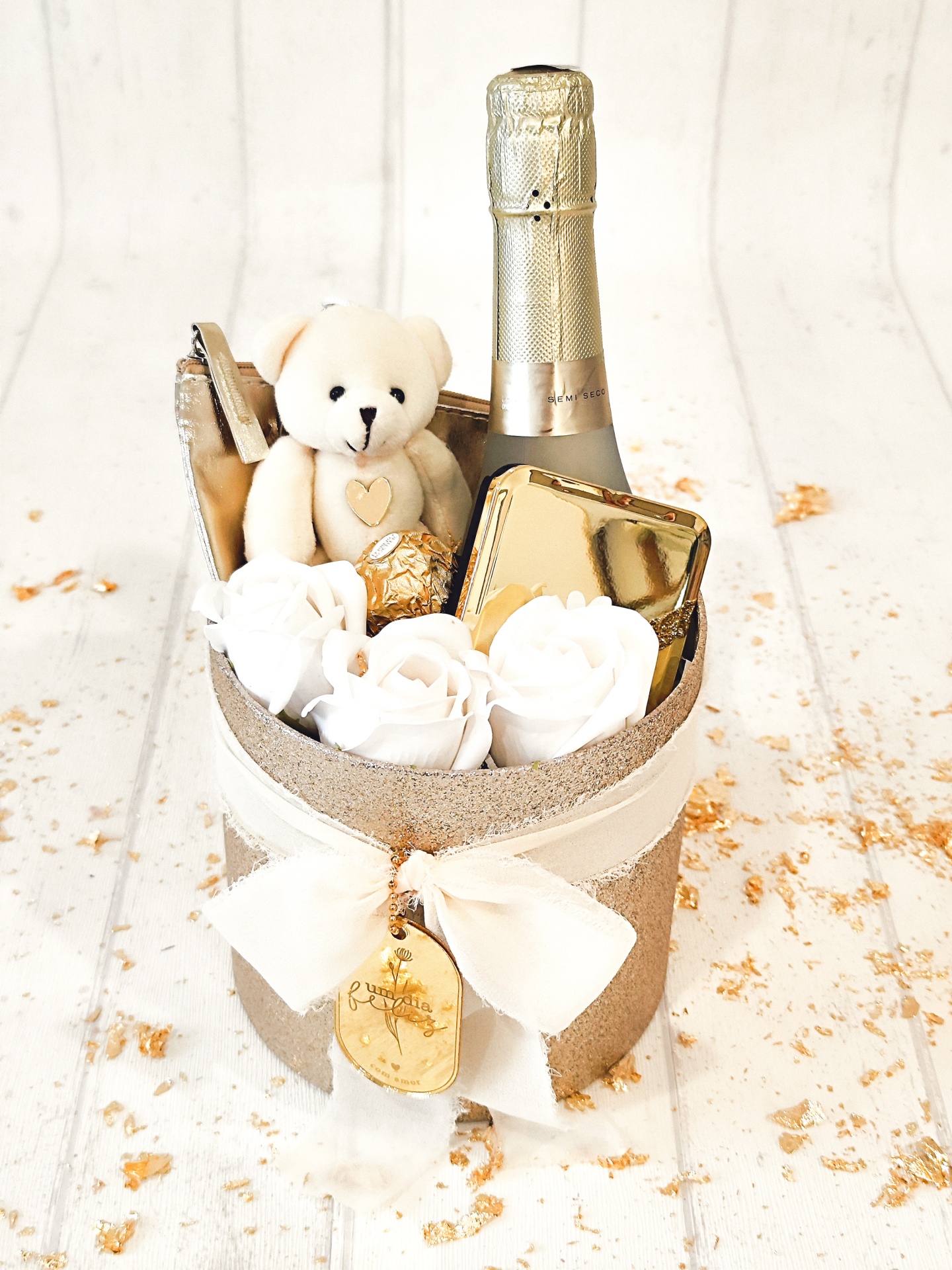 Conjunto de presente com ursinho, garrafa semi seco, rosas brancas e caixa dourada numa caixa dourada com laço branco.