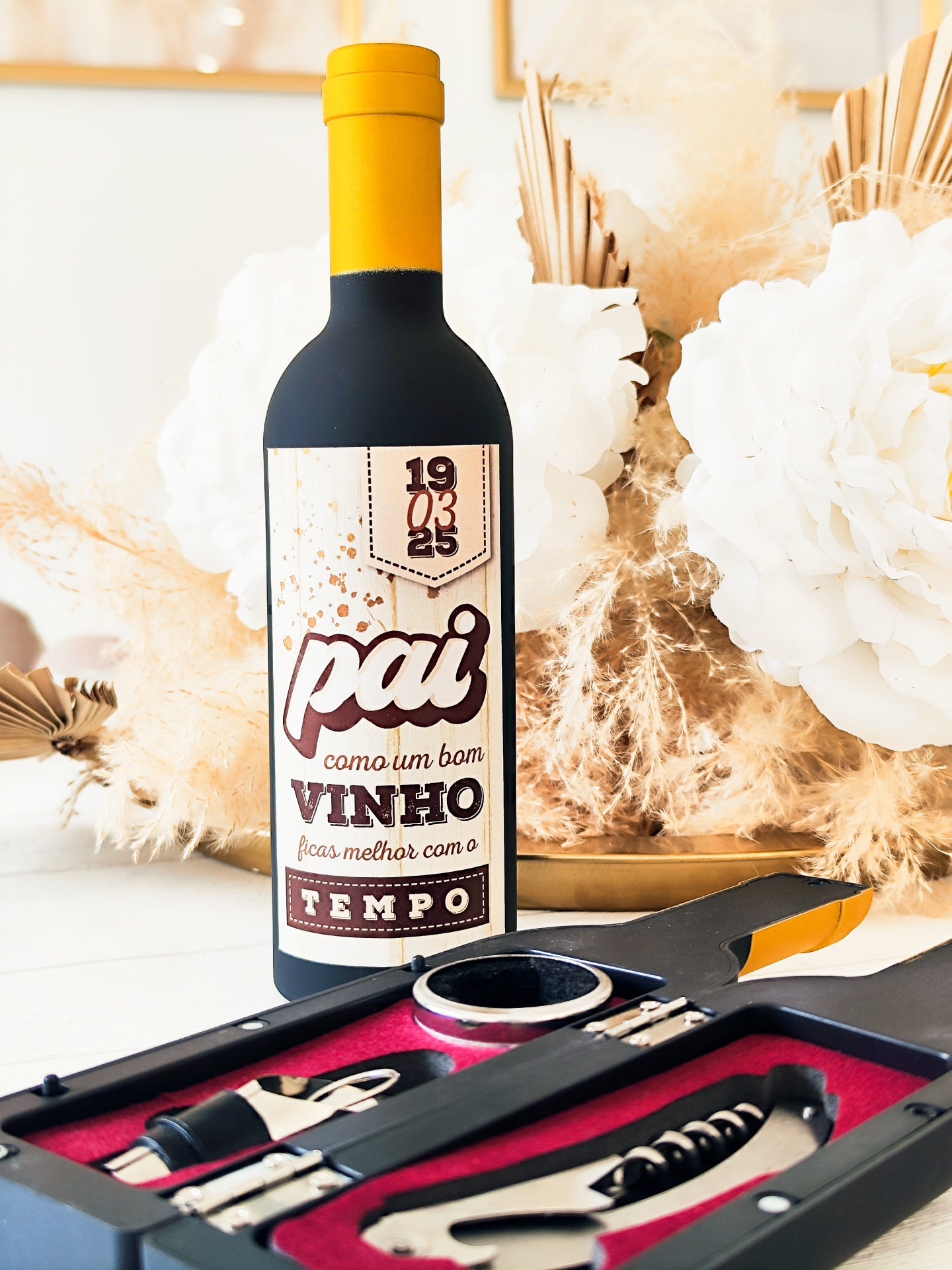 Garrafas de vinho com rótulo personalizado e acessórios para vinho próximos, decorados com flores brancas e sépia.