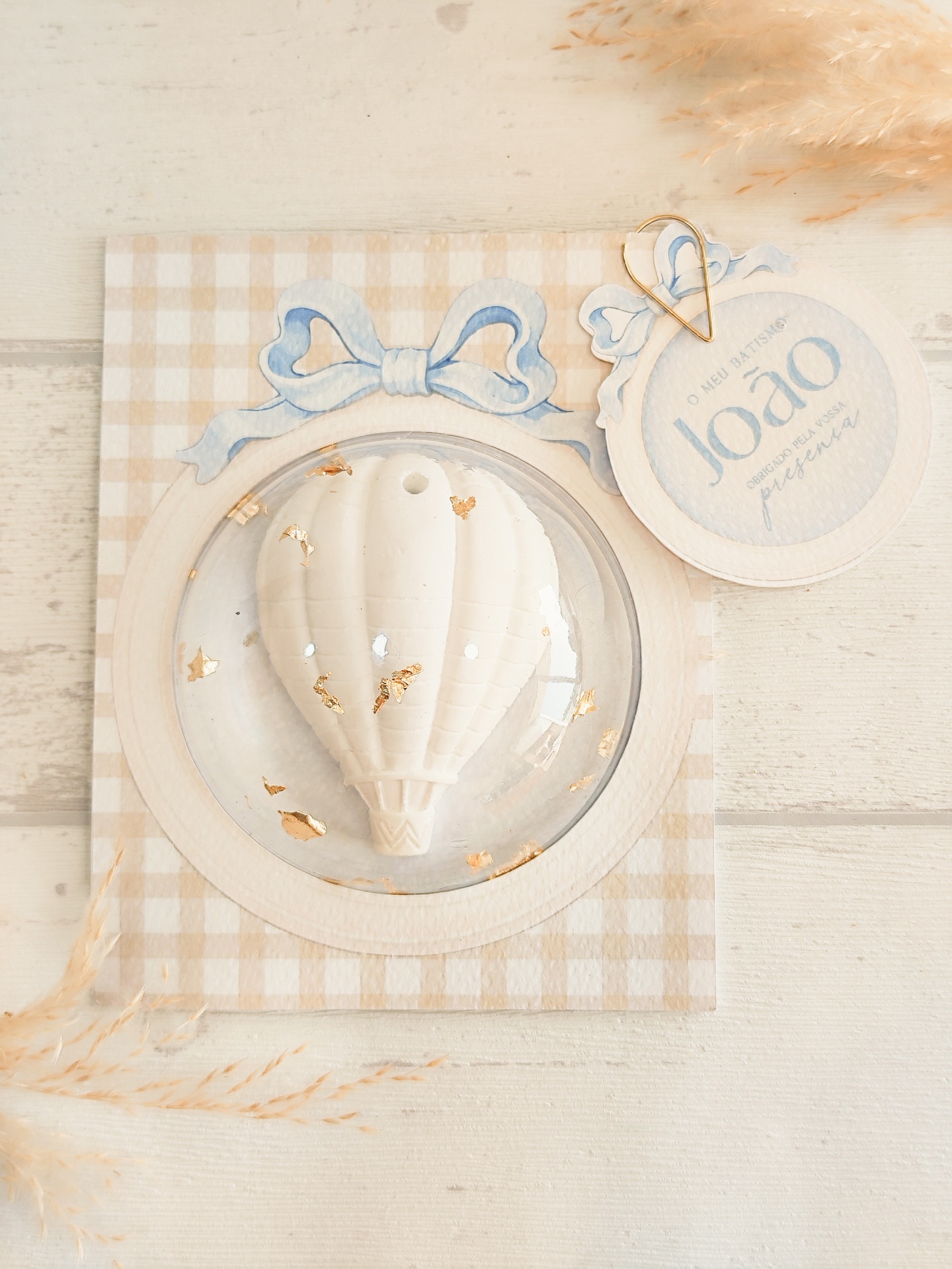 Produto decorativo balão branco com detalhes dourados em cartão xadrez bege e branco com etiqueta azul e branca.