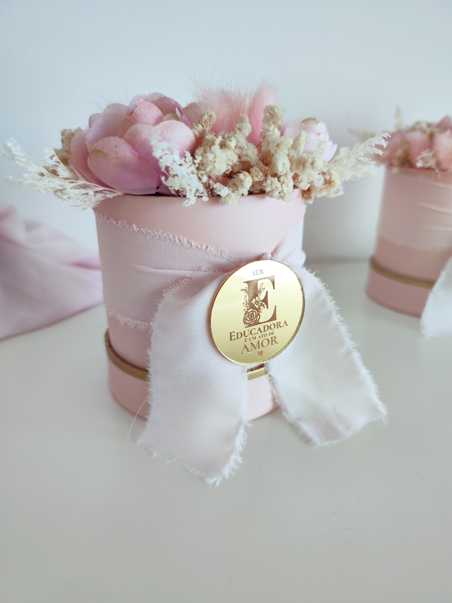 Vaso rosa claro com flores artificiais e placa dourada com texto