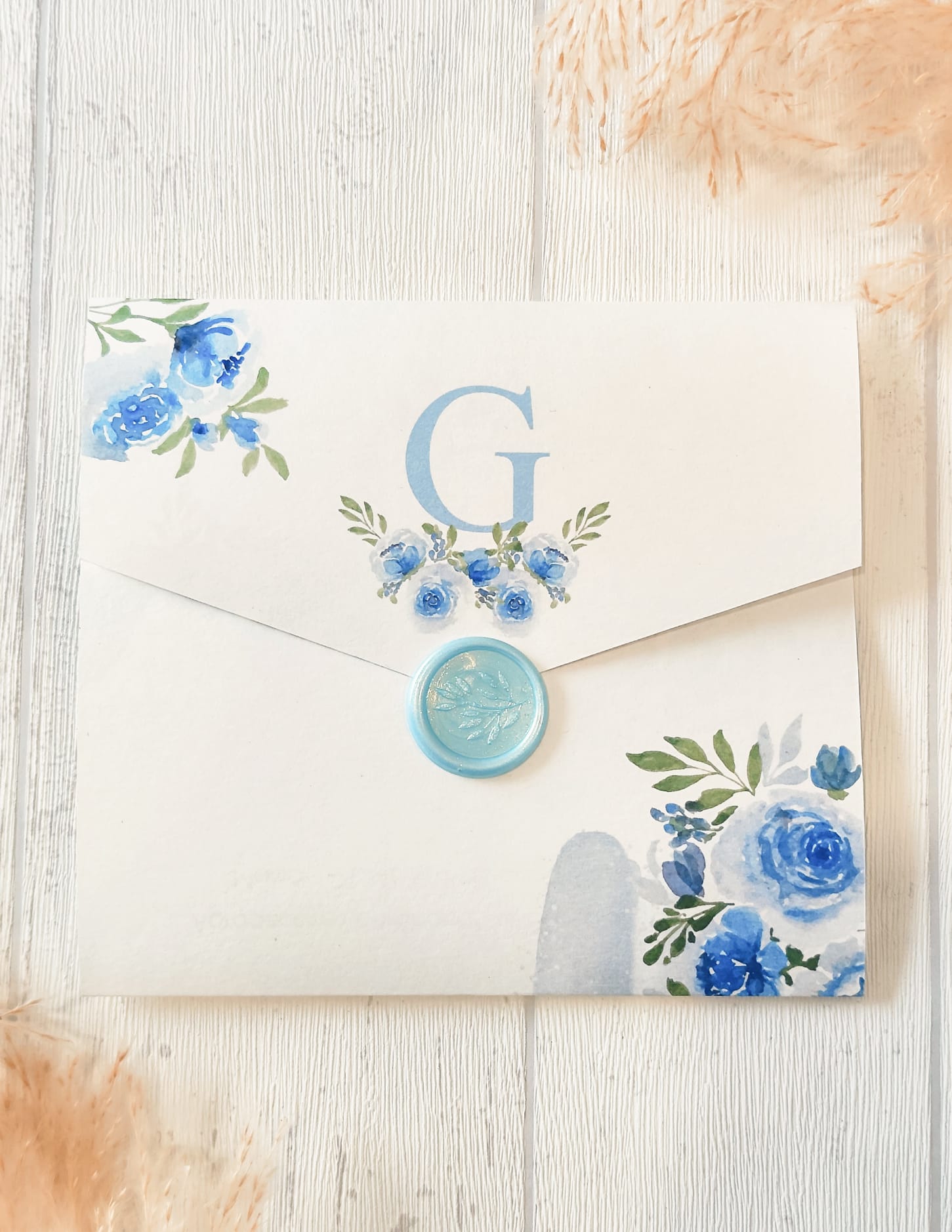 Envelope quadrado branco decorado com flores azuis e selo azul claro