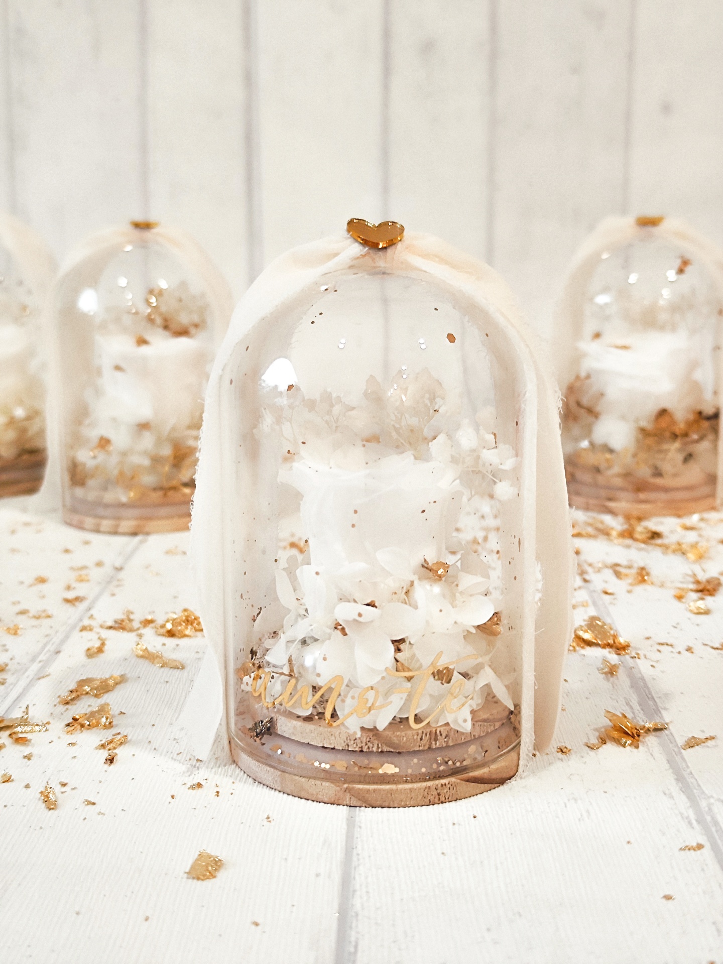 Vela decorativa branca com flores e glitter numa campânula transparente com base de madeira.