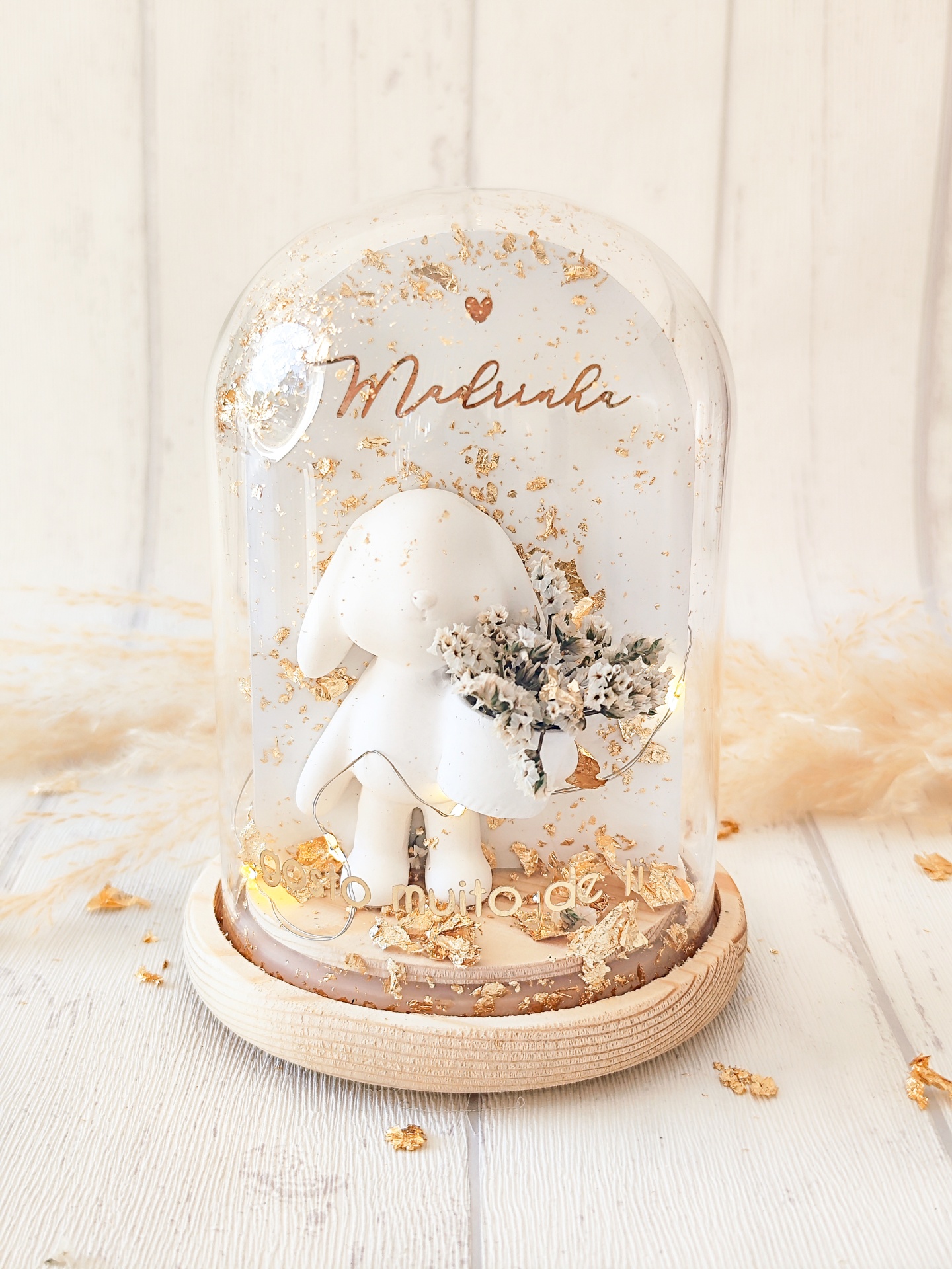 Peça decorativa de coelho branco com flores sob campânula de vidro com base de madeira e texto dourado