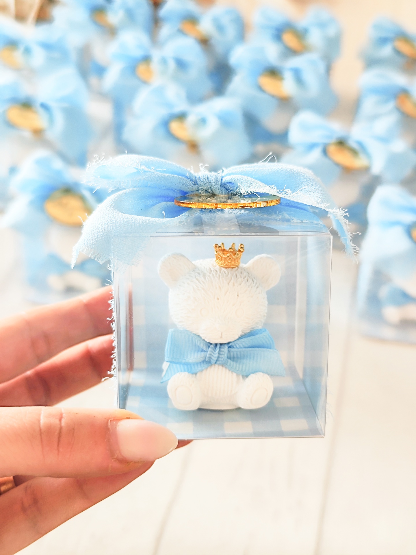 Figura de urso branco com coroa dourada e laço azul em caixa transparente com fita azul