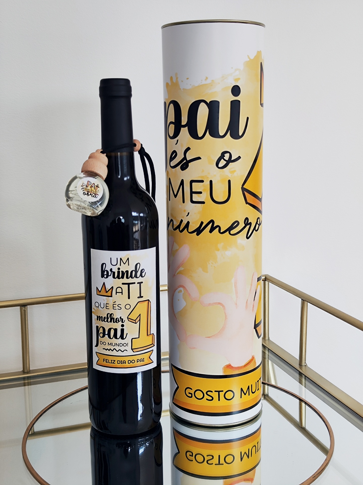 Garrafa de vinho com rótulo comemorativo para o Dia do Pai e embalagem cilíndrica ao lado, em mesa espelhada