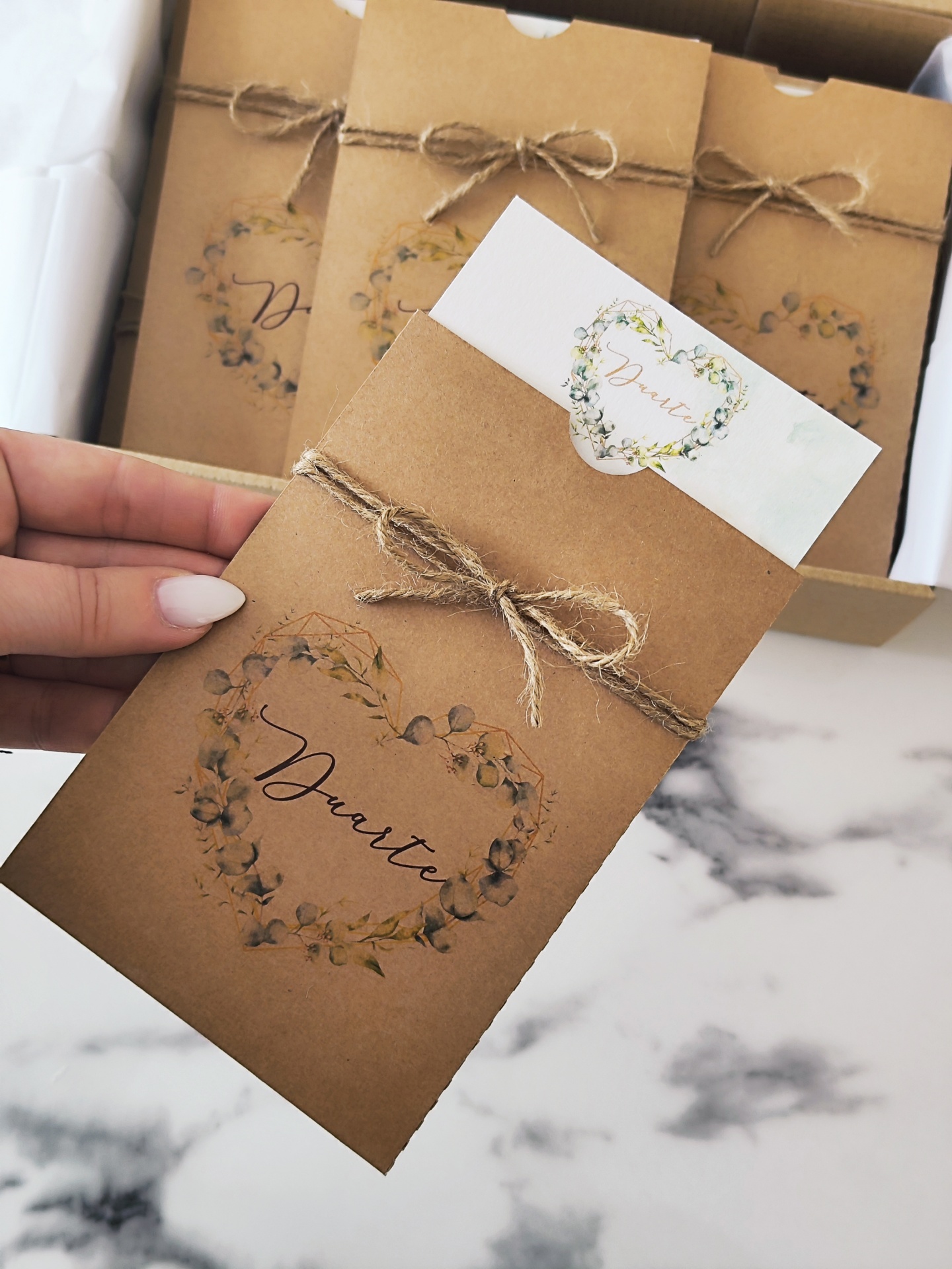 Envelope castanho com cordão e design floral, com cartão branco e nome Duarte
