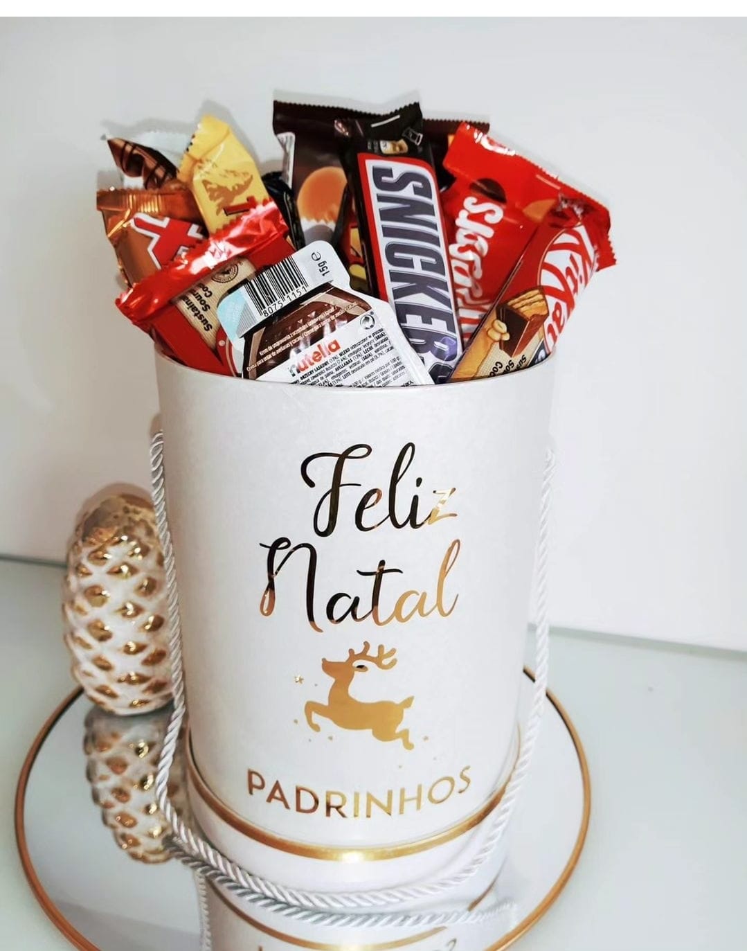 Recipiente branco com doces e decoração natalícia ao lado de objeto decorativo branco e dourado