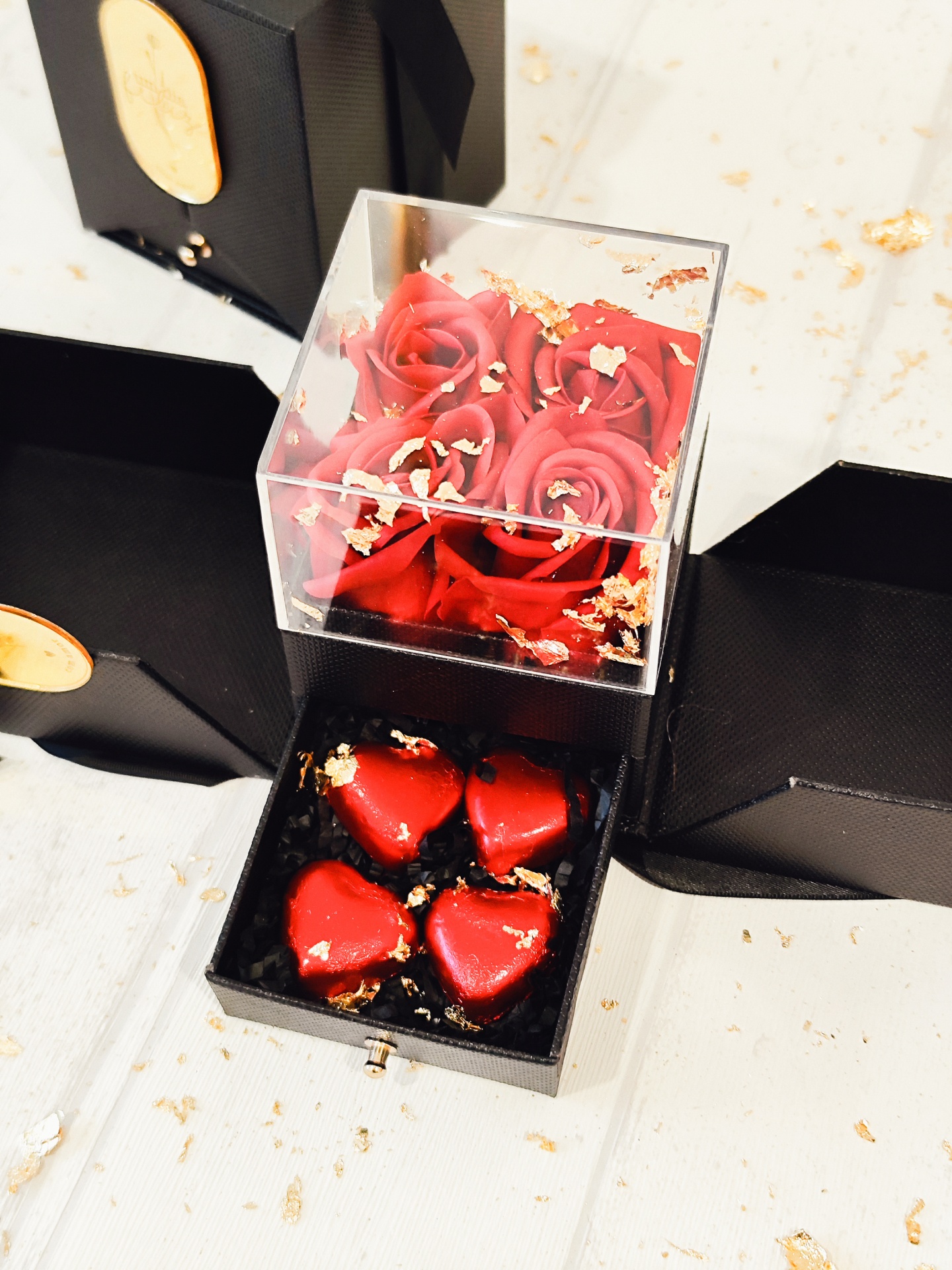Caixa preta com rosas vermelhas artificiais e bombons vermelhos em forma de coração