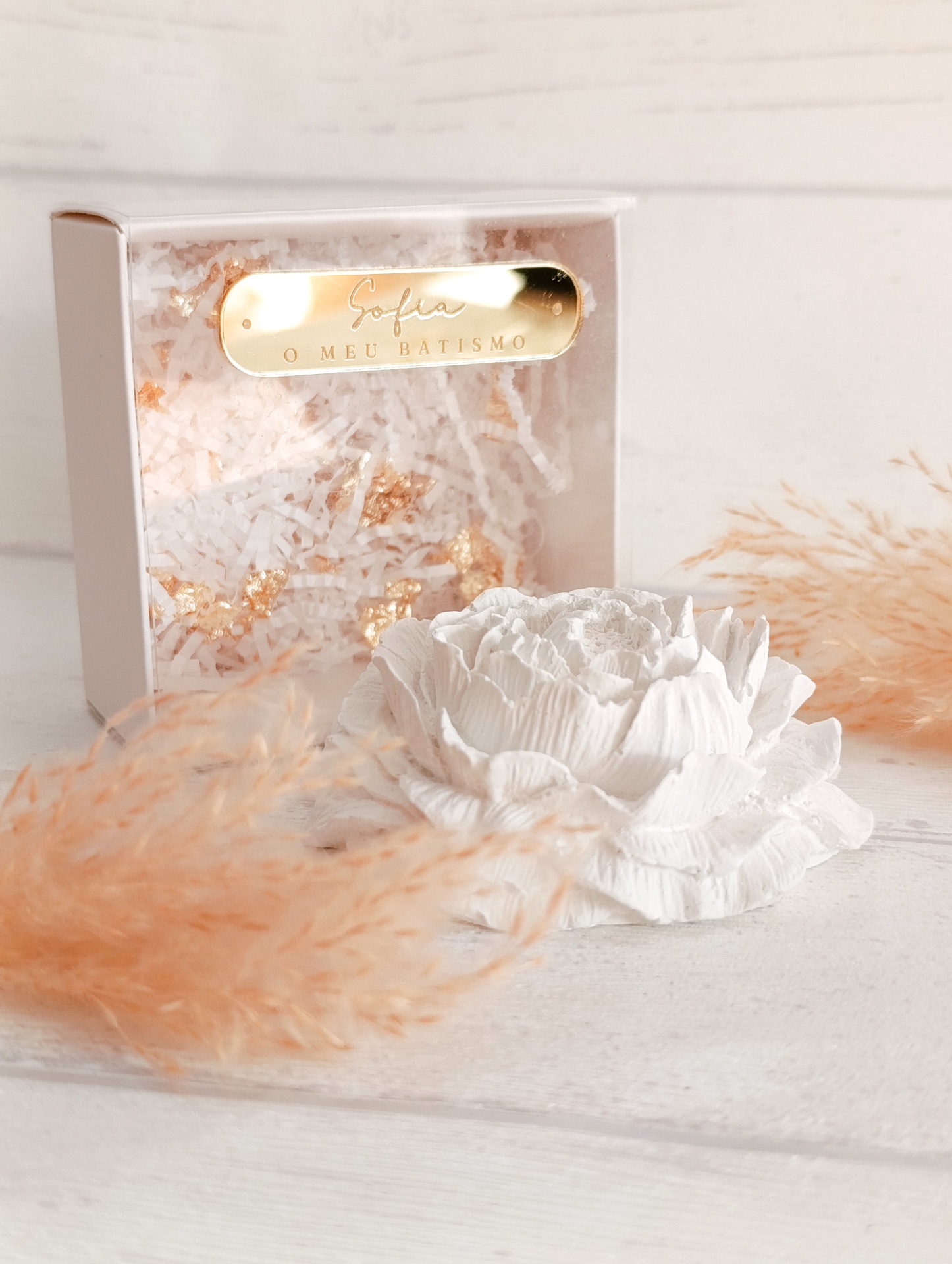 Flor decorativa branca em relevo com caixa branca de papel picado e placa dourada com texto