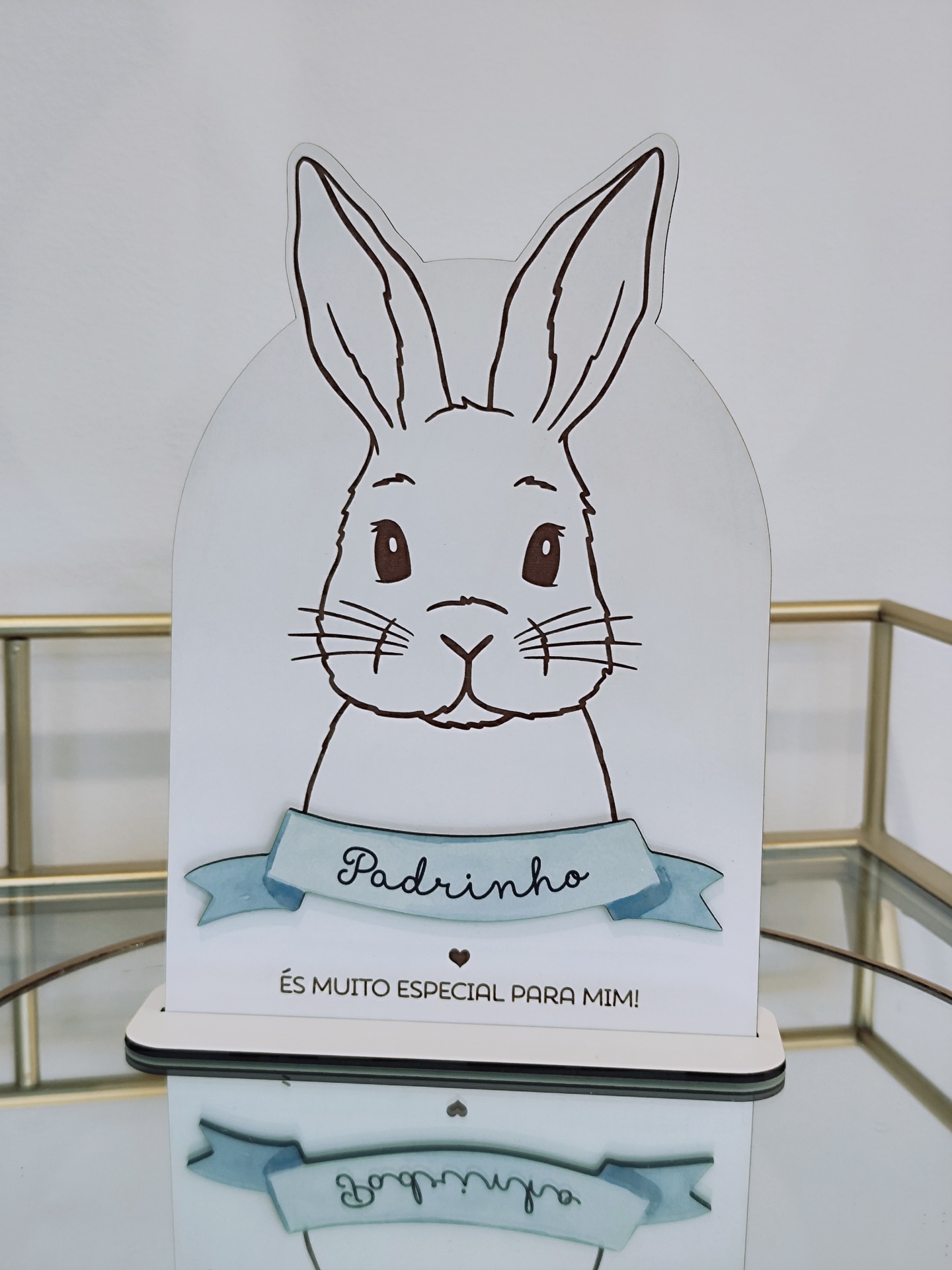 Objeto decorativo em forma de coelho com texto 'Padrinho' e 'ÉS MUITO ESPECIAL PARA MIM!' sobre superfície de vidro
