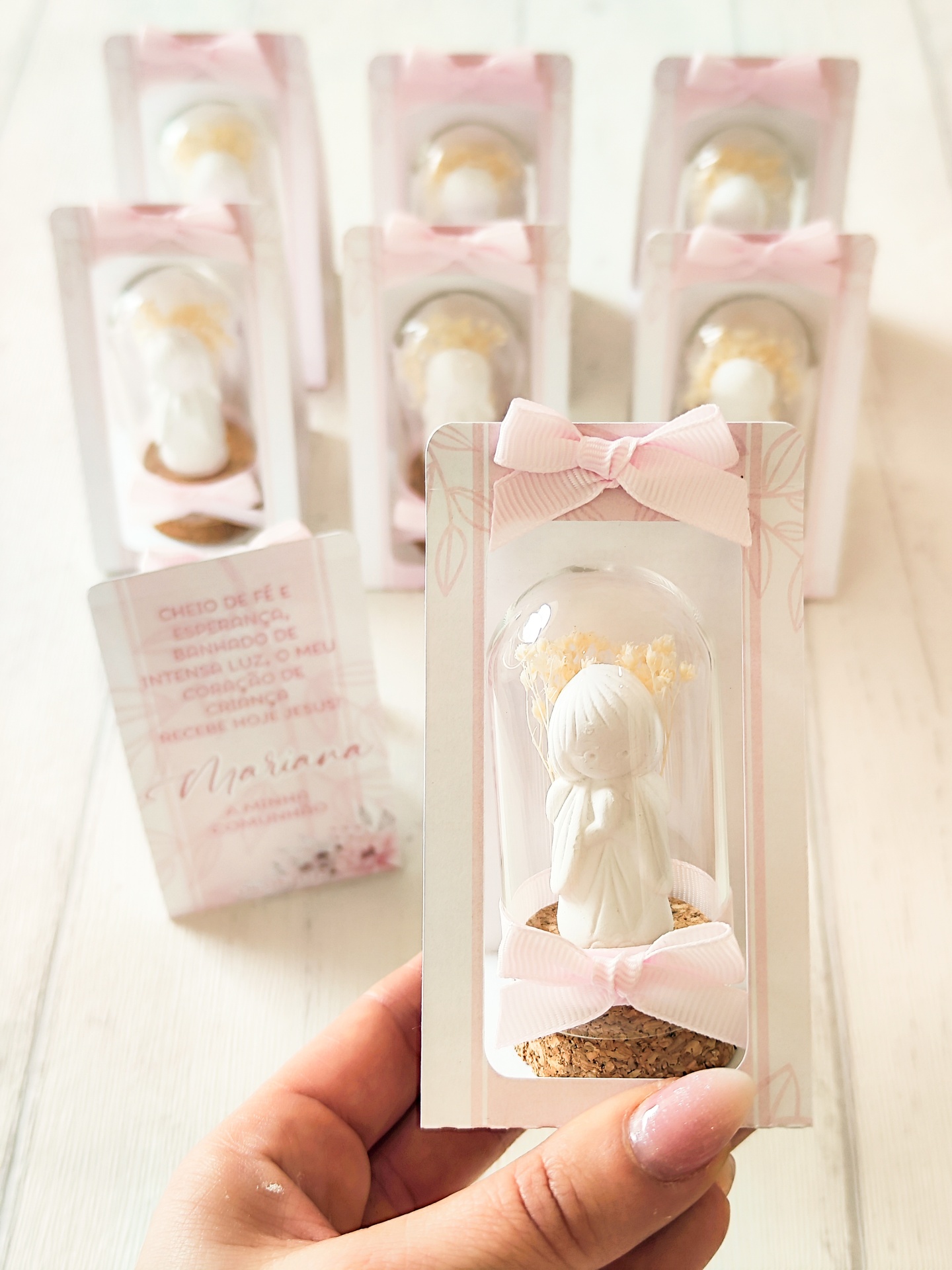 Miniatura decorativa de anjo branco dentro dunha cápsula de vidro con flores secas amarelas e lazos rosas