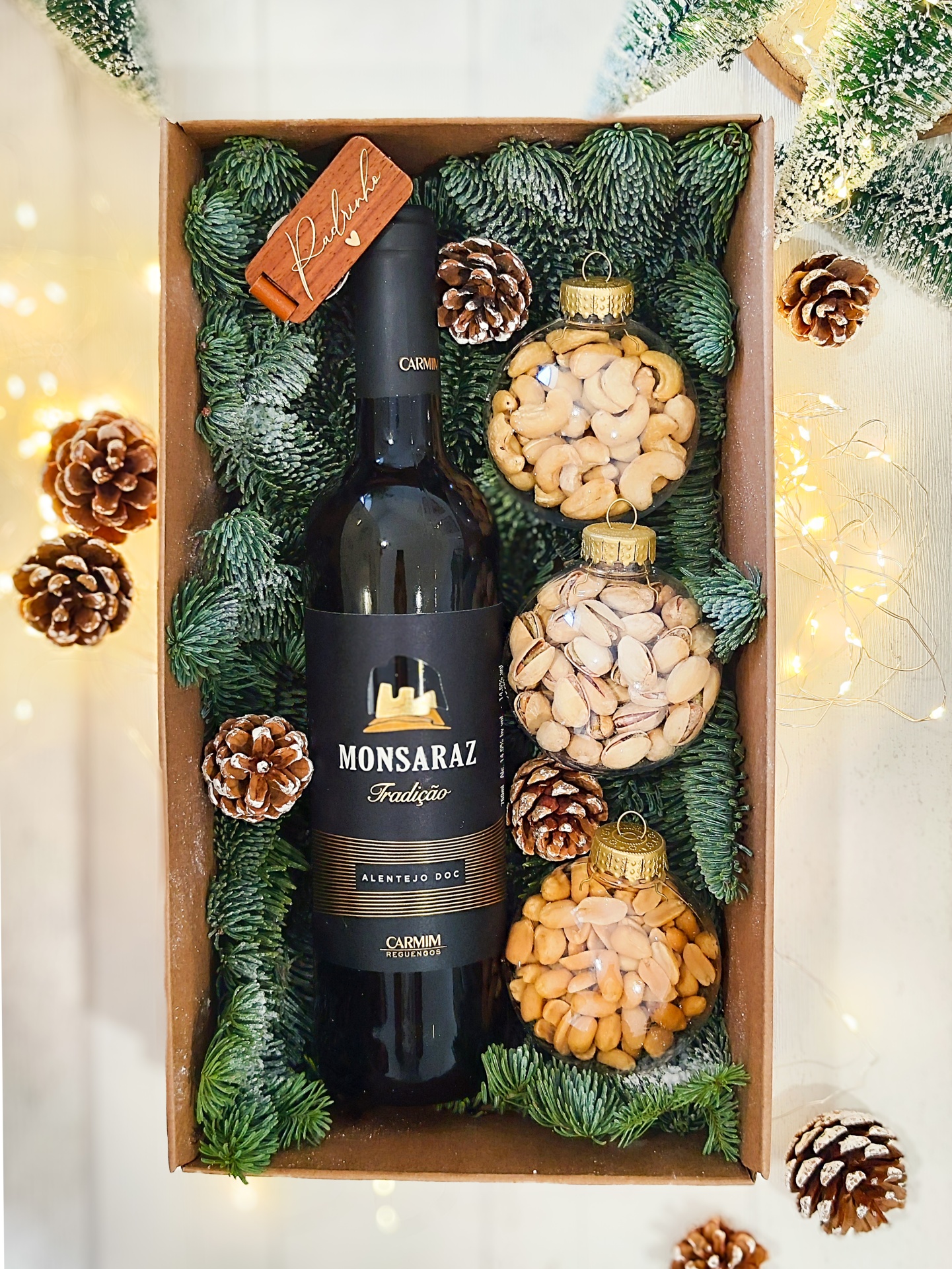 Conjunto de presente com garrafa de vinho e bolas decorativas de frutos secos em caixa com decoração de pinhas e ramos verdes