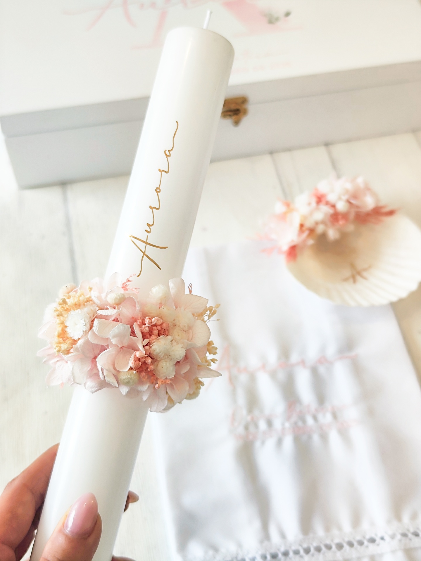 Vela branca decorada com coroa de flores e nome Aurora em dourado