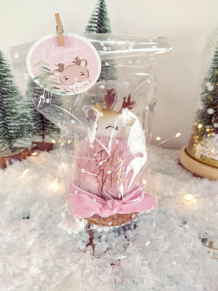 Pinheiro decorativo rosa com chifres dourados em embalagem plástica com etiqueta 'Obrigado' em fundo de neve artificial e árvores de Natal.