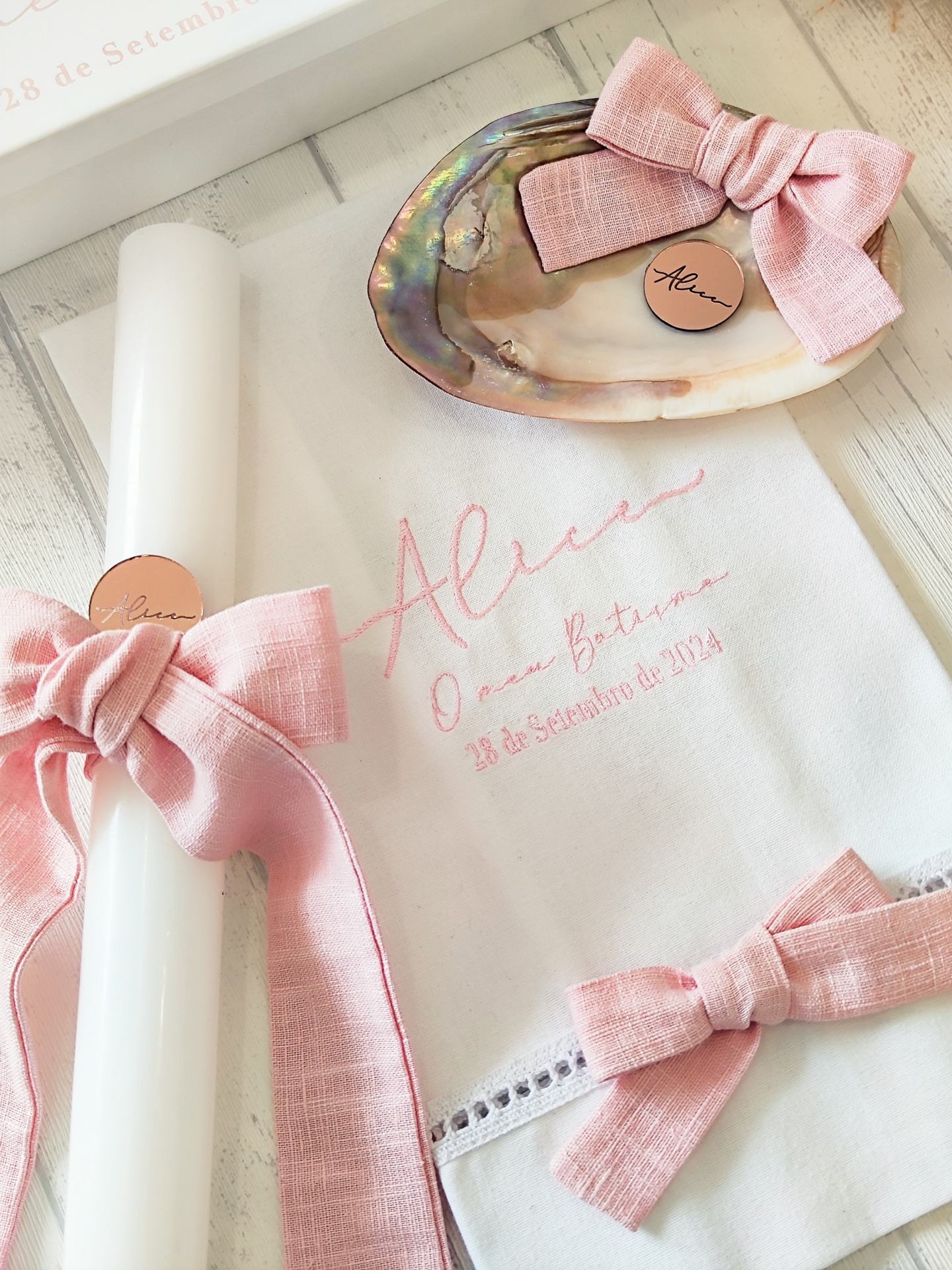 Toalha branca bordada com nome e data, vela branca e concha com laço rosa