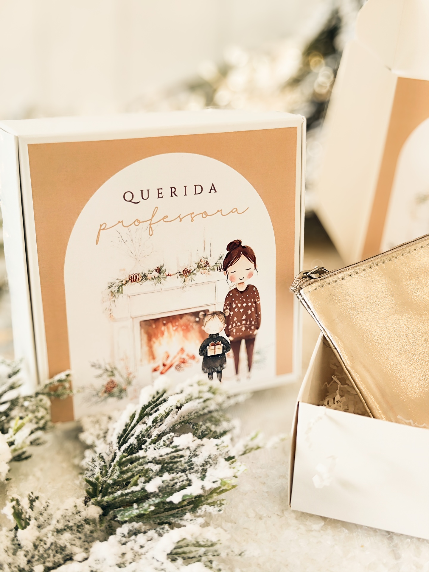 Caixa decorativa com ilustração e texto para professora junto a mala dourada e neve falsa