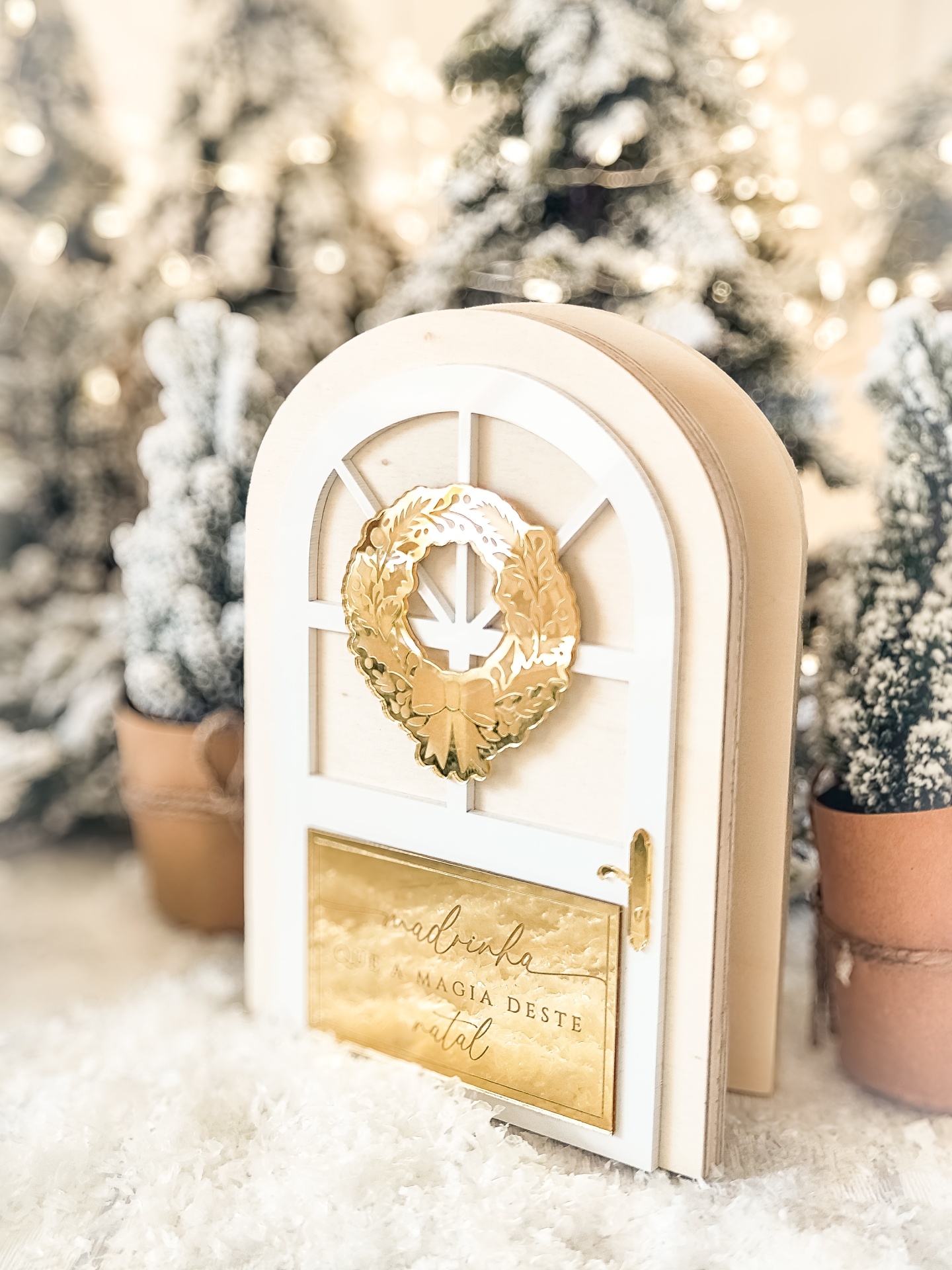 Porta decorativa branca com coroa dourada e placa com texto em cenário de Natal