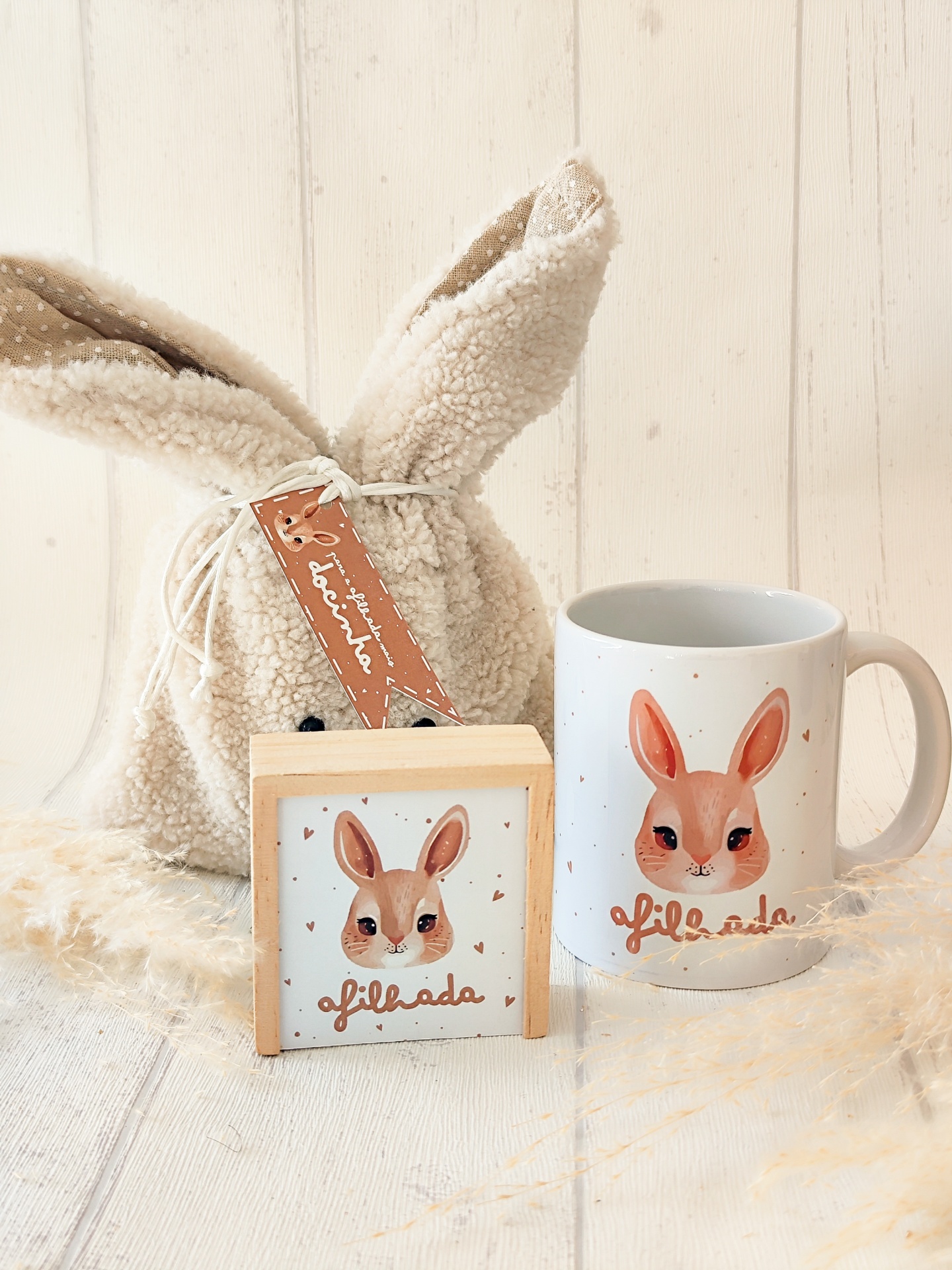 Conjunto com caneca, quadro e bolsa de pelúcia com imagem e texto de coelho e palavra 'afilhada'.