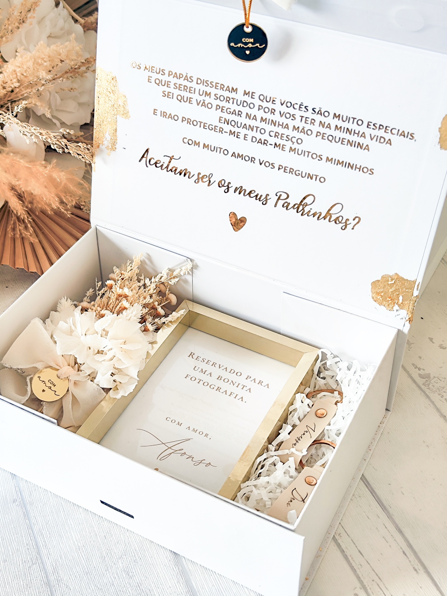 Caixa decorativa branca com moldura dourada, raminhos secos e etiqueta preta com texto em dourado