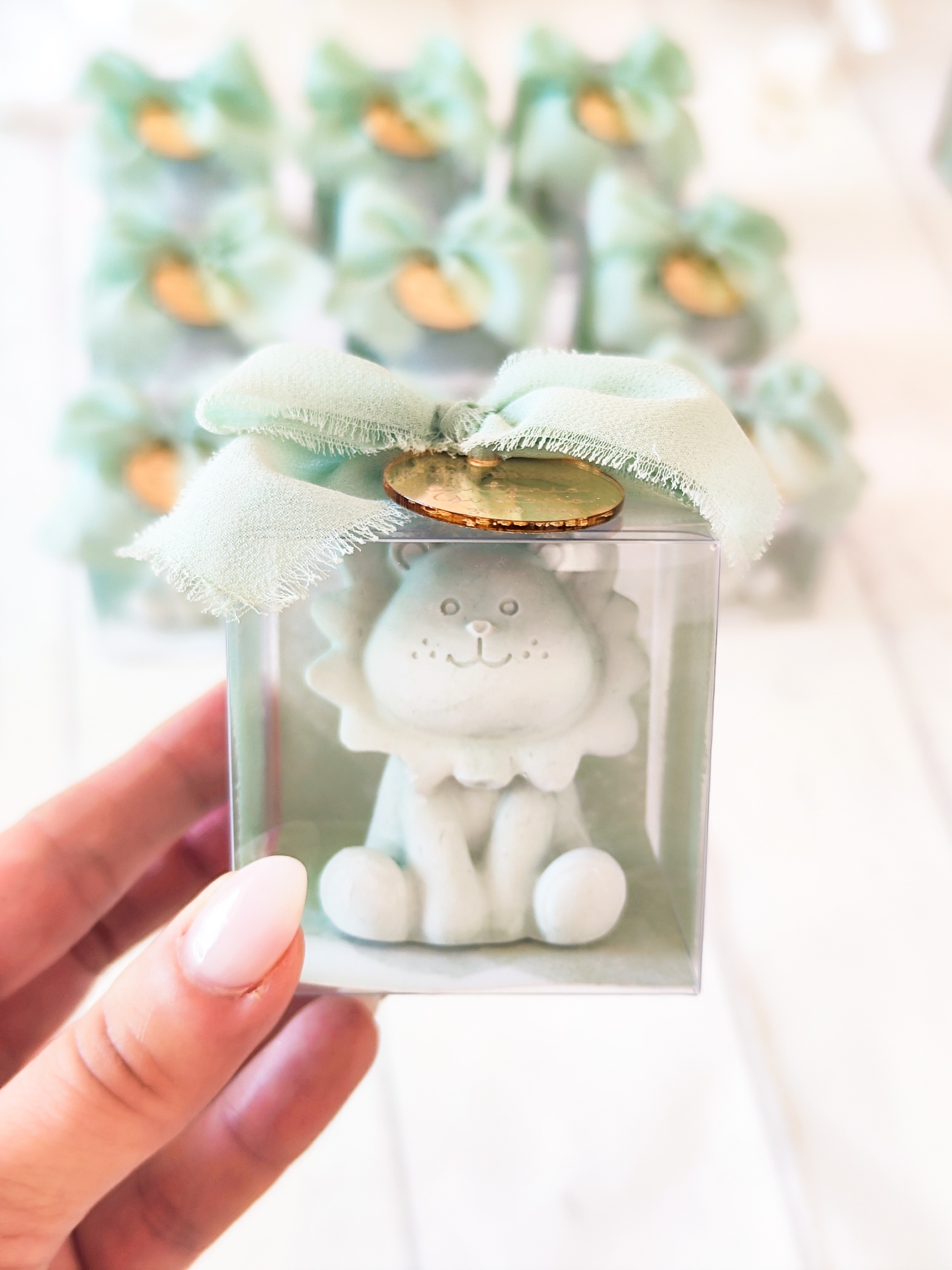 Pequena figura de leão branco numa caixa transparente com laço verde e medalha dourada