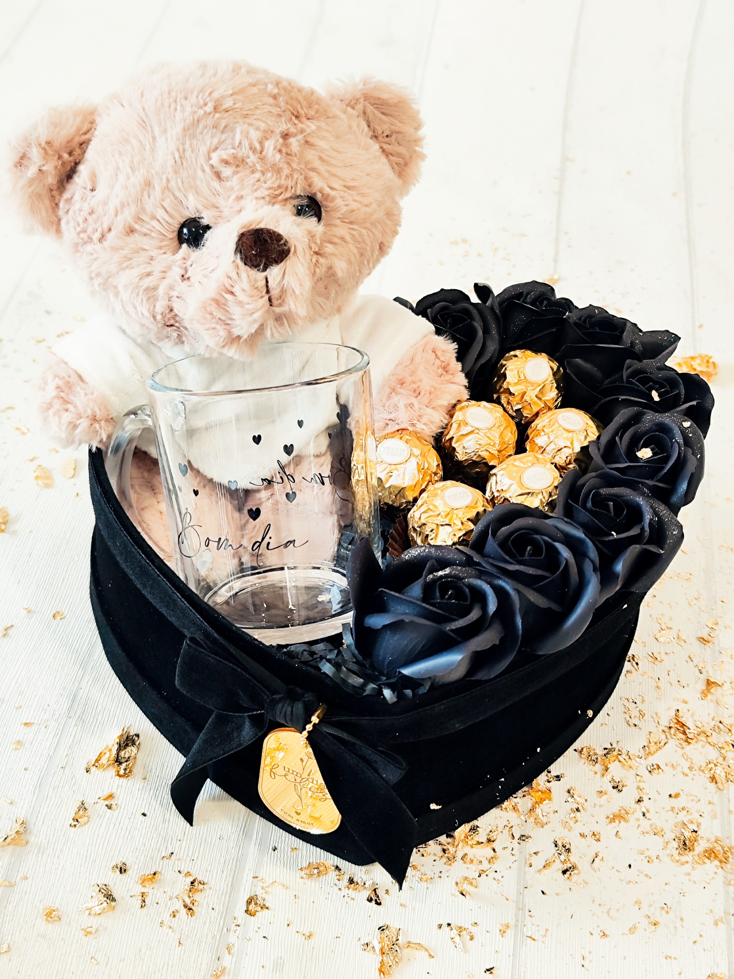 Caixa em forma de coração com ursinho de peluche, copo de vidro, rosas pretas artificiais e bombons dourados