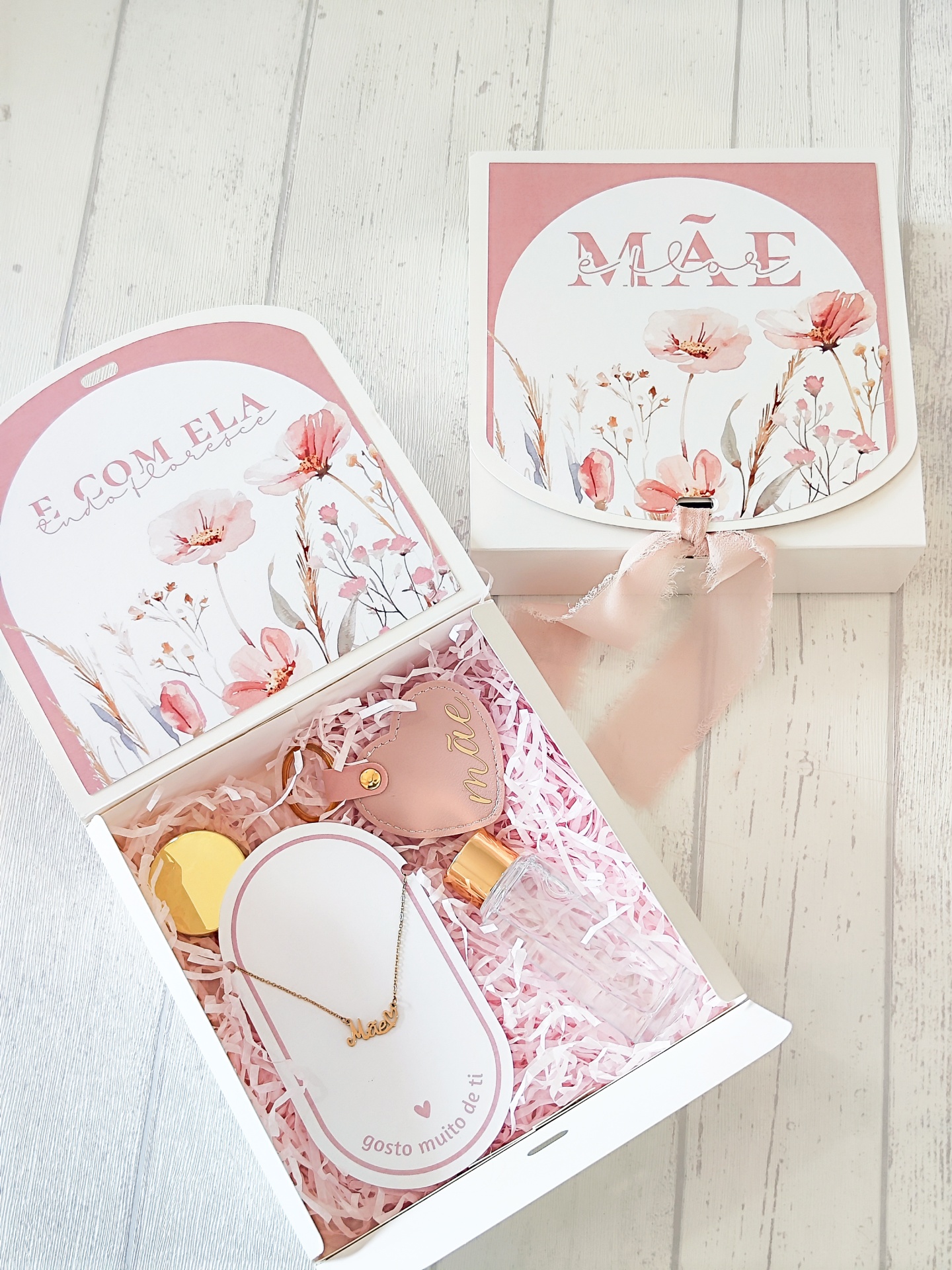 Caixa de presente branca com decoração floral e itens de joalharia e perfume.