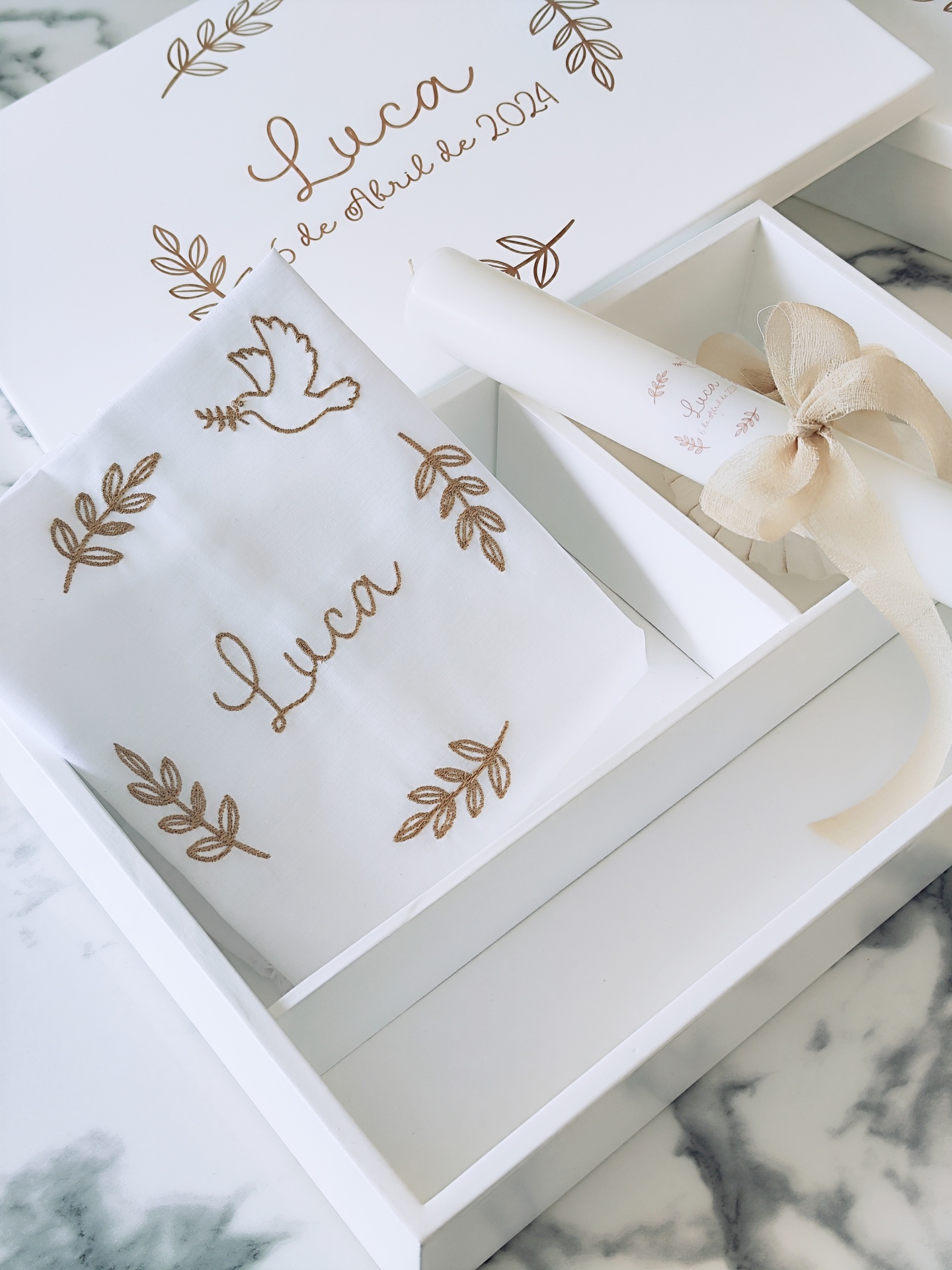 Conjunto de batismo com tecido branco bordado, caixa branca decorada e rolo de papel com fita bege