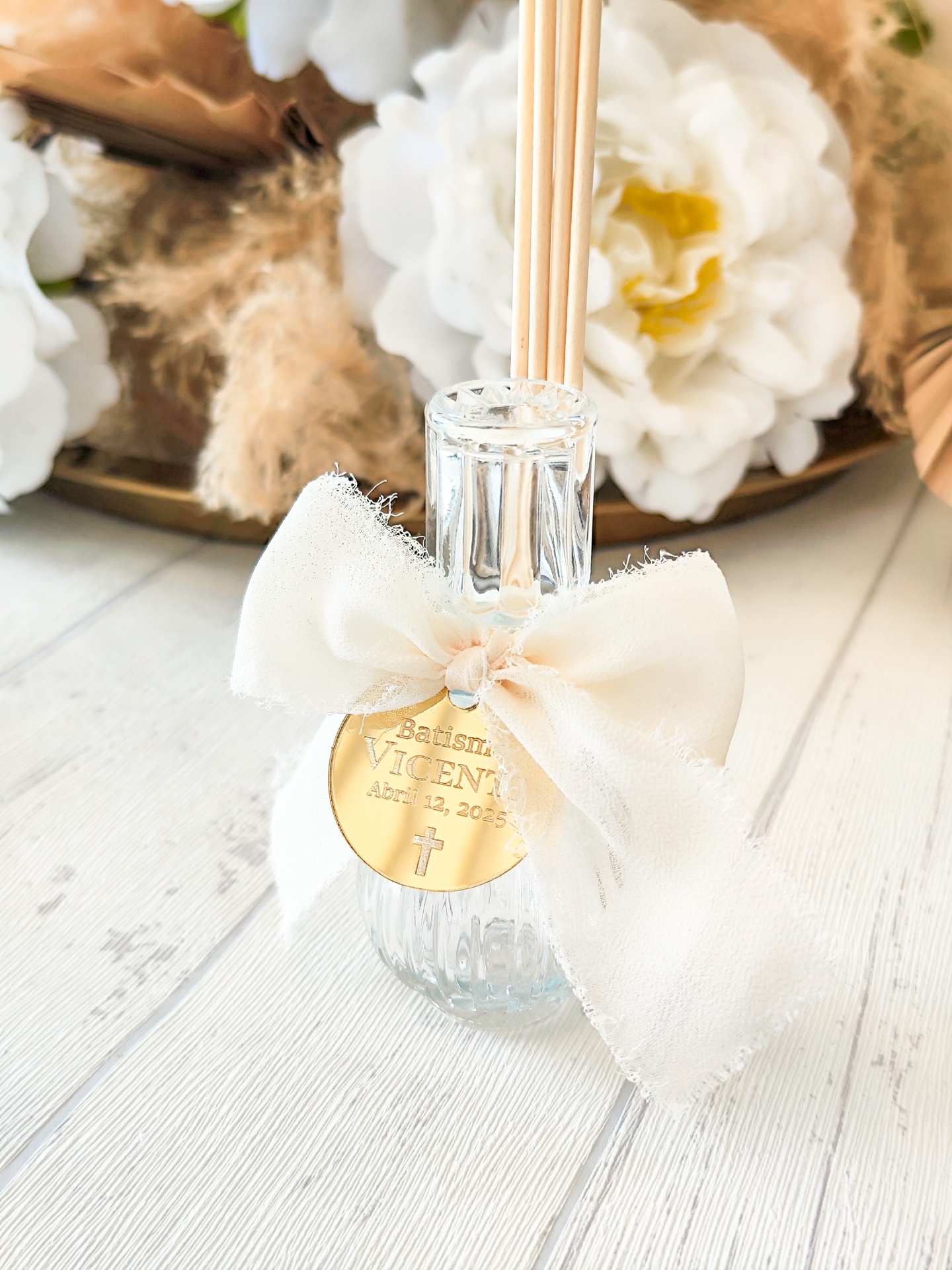 Difusor de fragrância com laço branco e etiqueta dourada em superfície de madeira clara