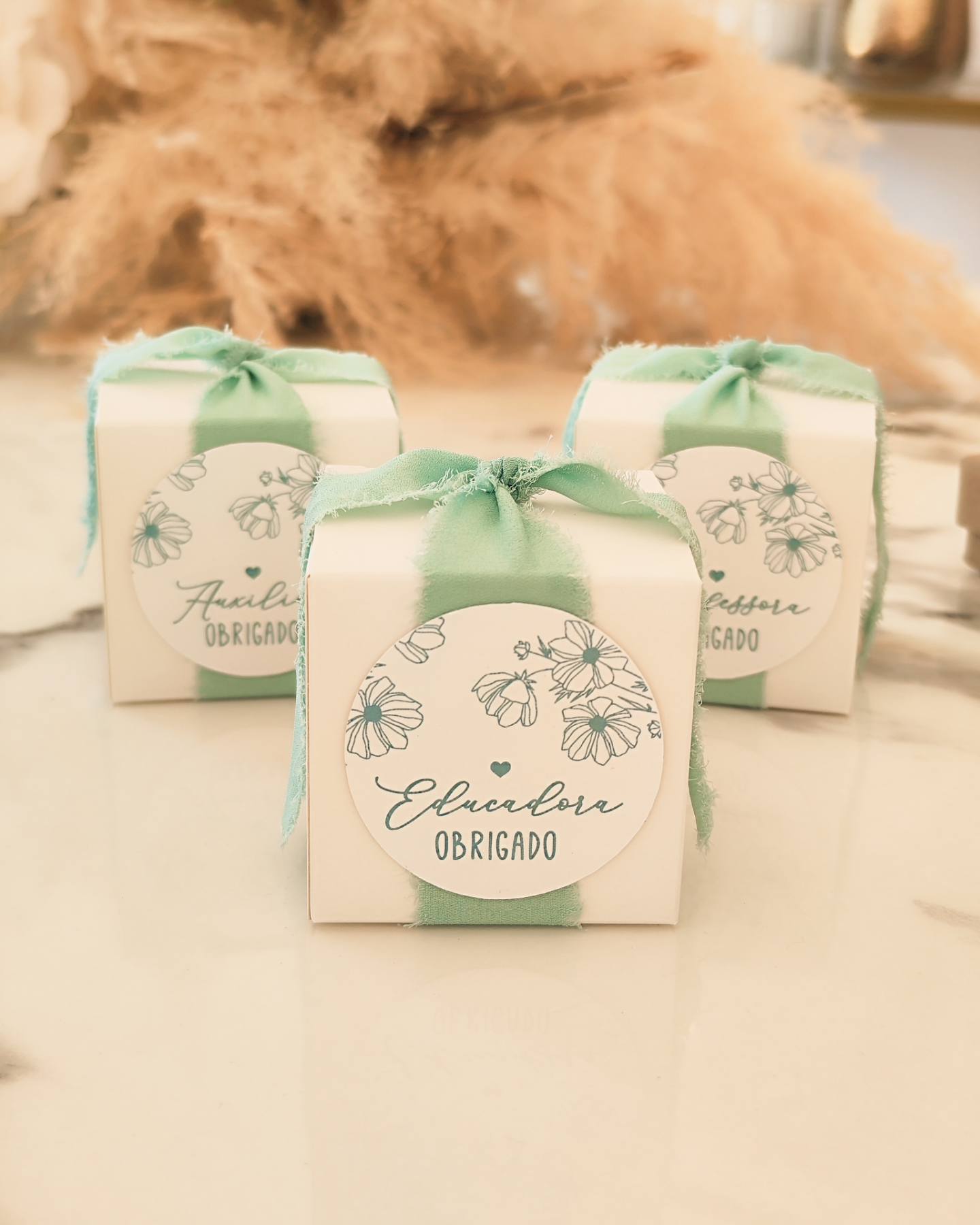 Caixas brancas pequenas com fita verde e etiquetas florais com texto de agradecimento