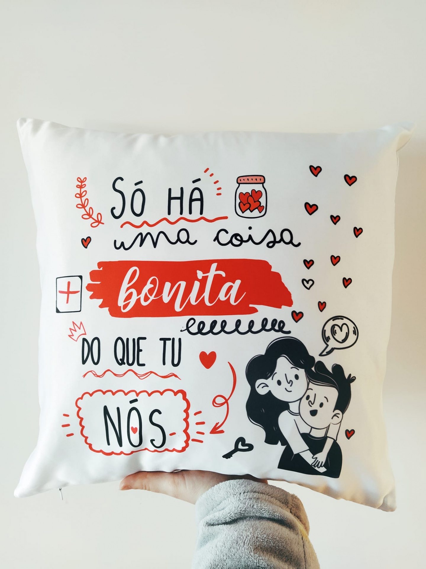 Almofada branca com texto e ilustração a preto e vermelho com casal e corações