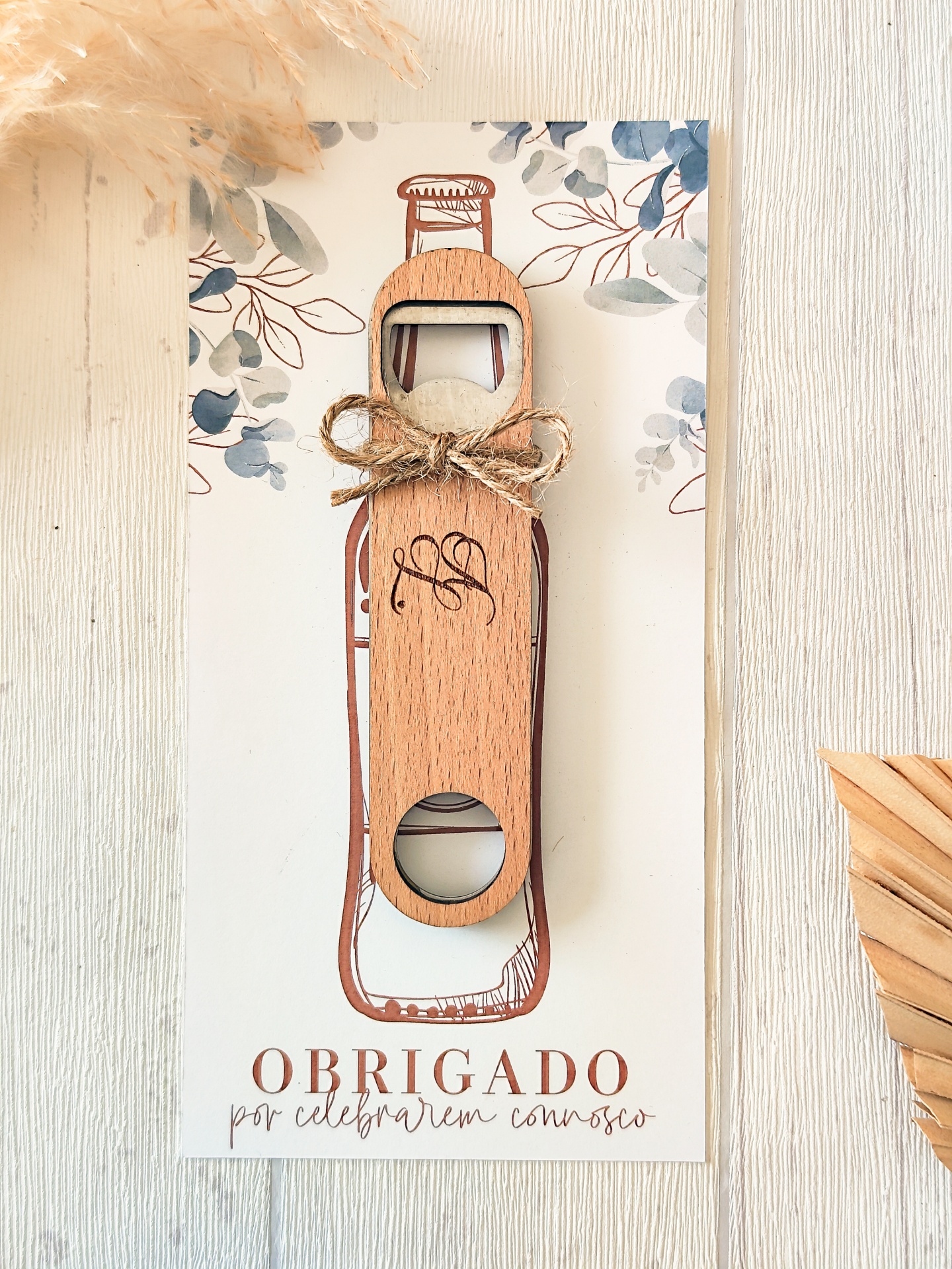 Abridor de garrafas de madeira com laço, colocado sobre cartão decorativo com texto de agradecimento
