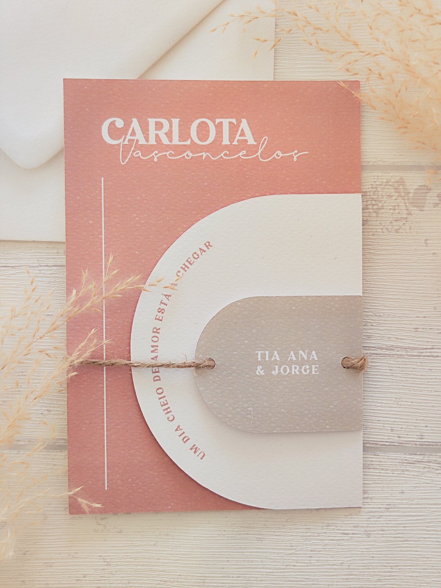 Convite texturizado rosa e bege com cordão e texto impresso, envelope branco ao fundo