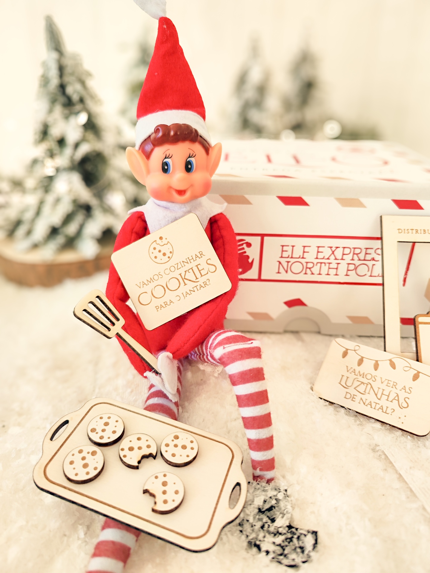 Boneco elfo de Natal com chapéu vermelho e branco sentado na neve com placa e bandeja de bolachas