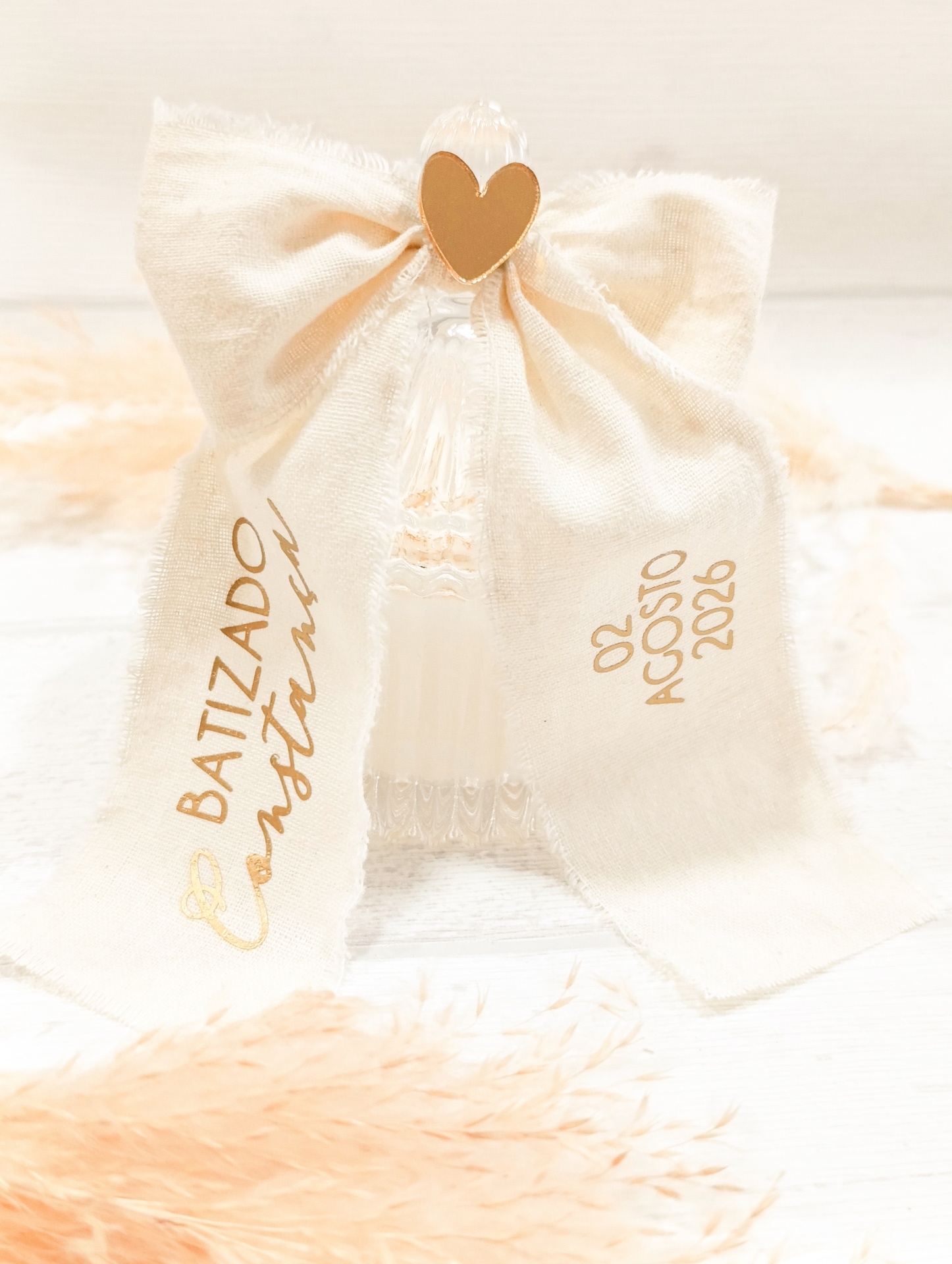 Garrafa de vidro com laço bege e texto dourado para batizado