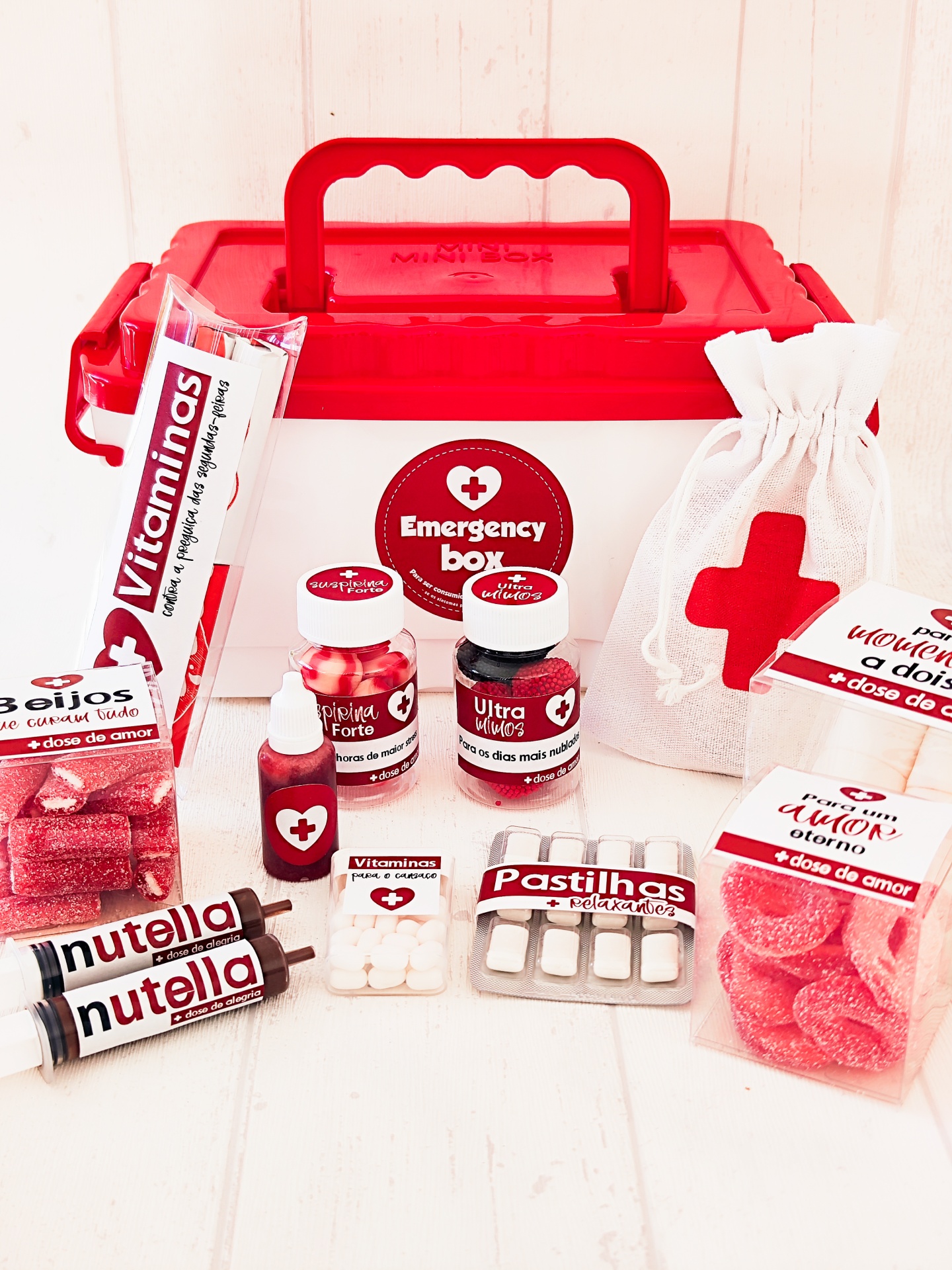 Caixa de emergência vermelha com produtos vários à volta sobre superfície branca