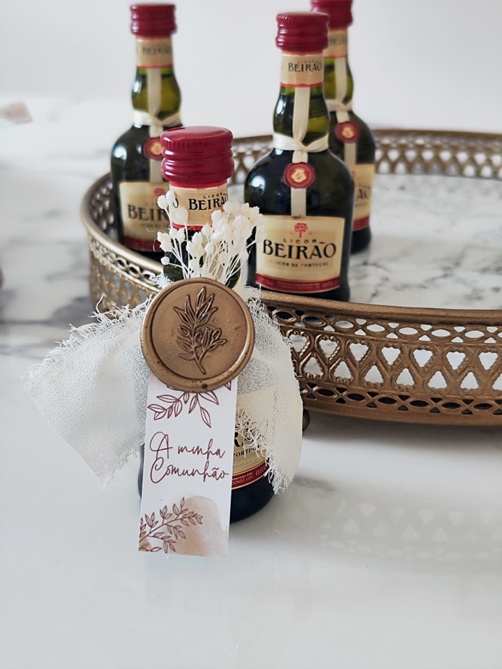 Mini garrafas de licor Beirão decoradas e colocadas numa bandeja dourada sobre mesa branca