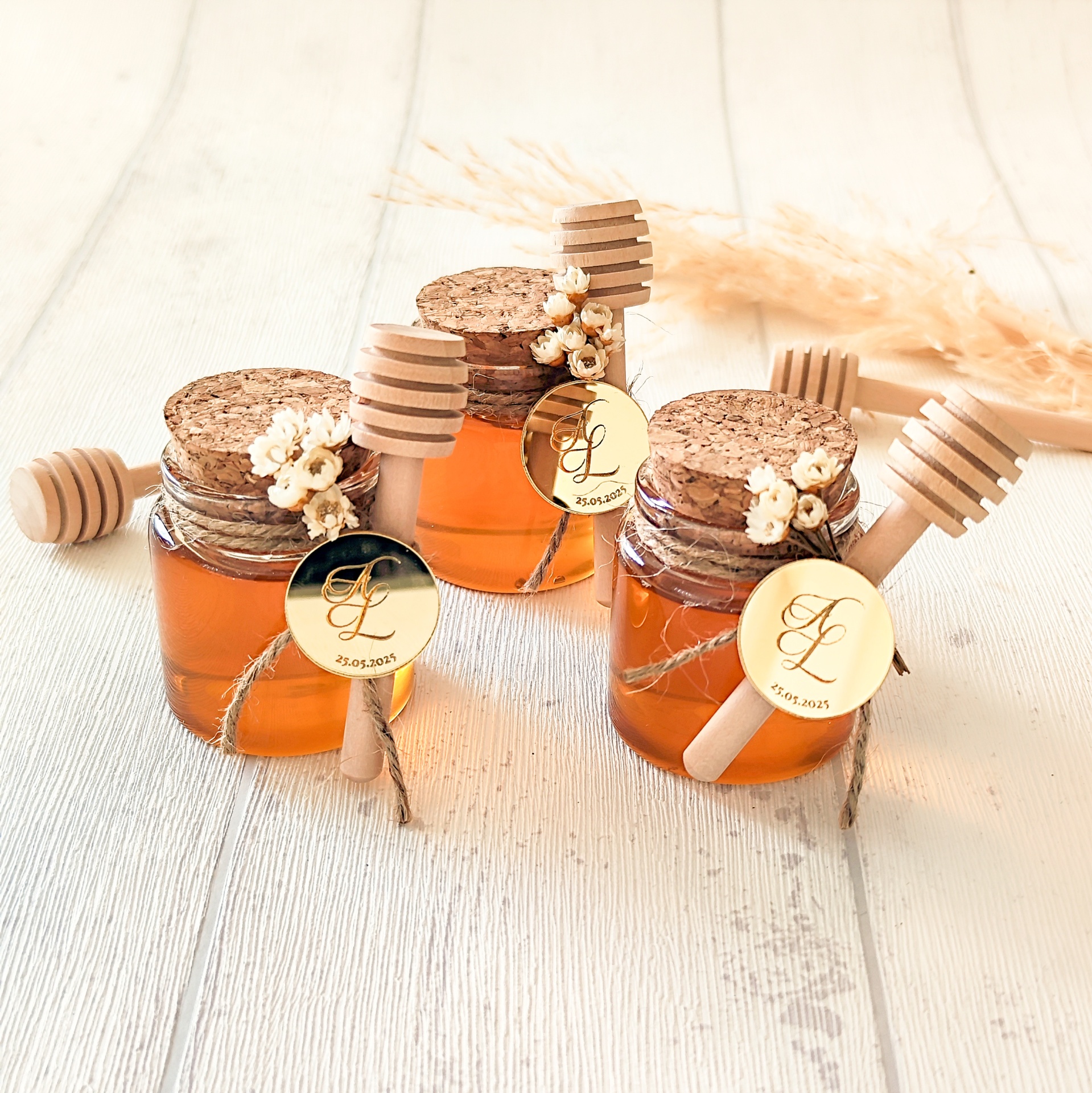 Frascos pequenos de vidro com mel, tampa de cortiça e mexedor de mel de madeira.